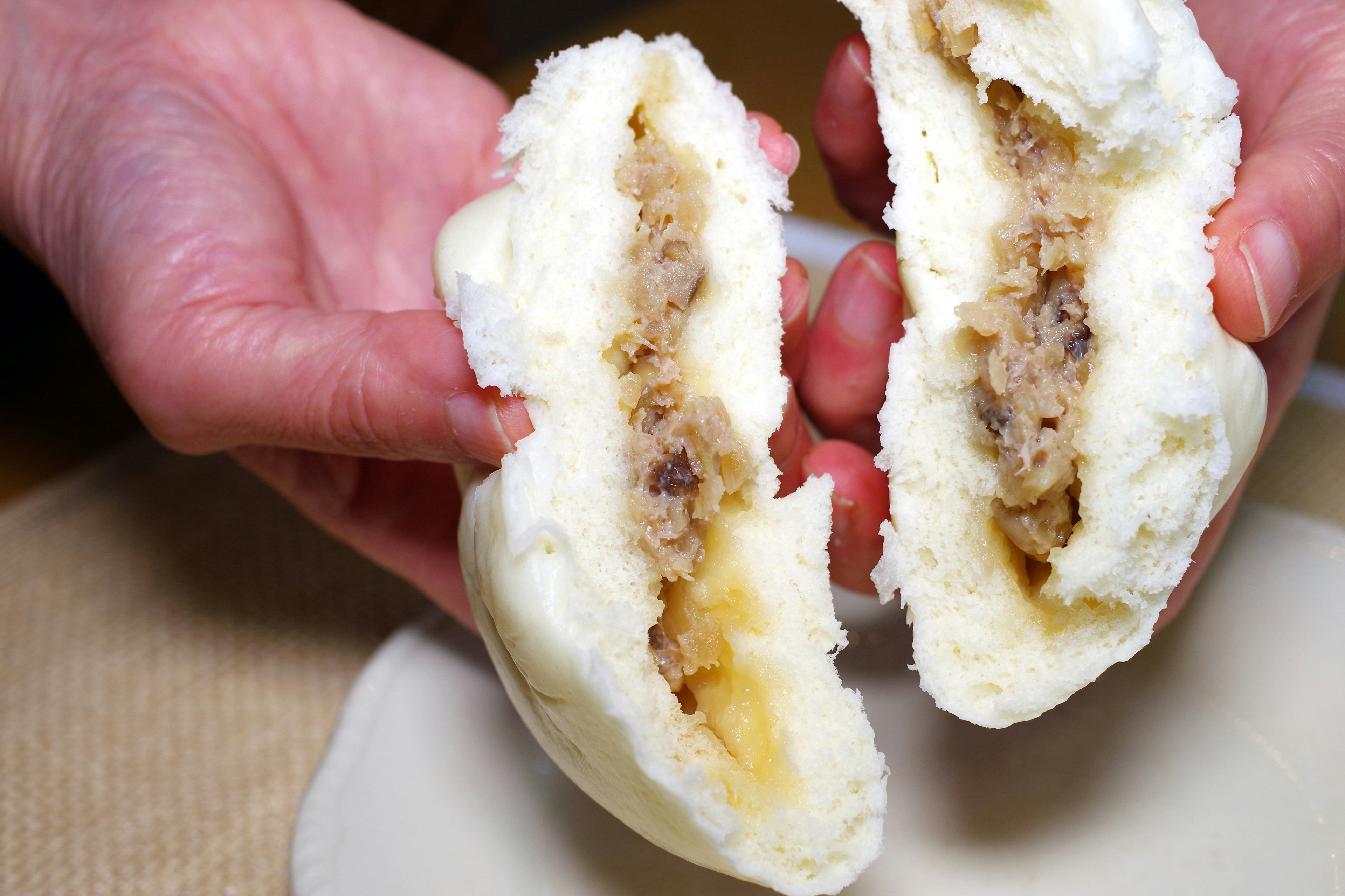 Two white steamed buns held in hands showing the filling inside