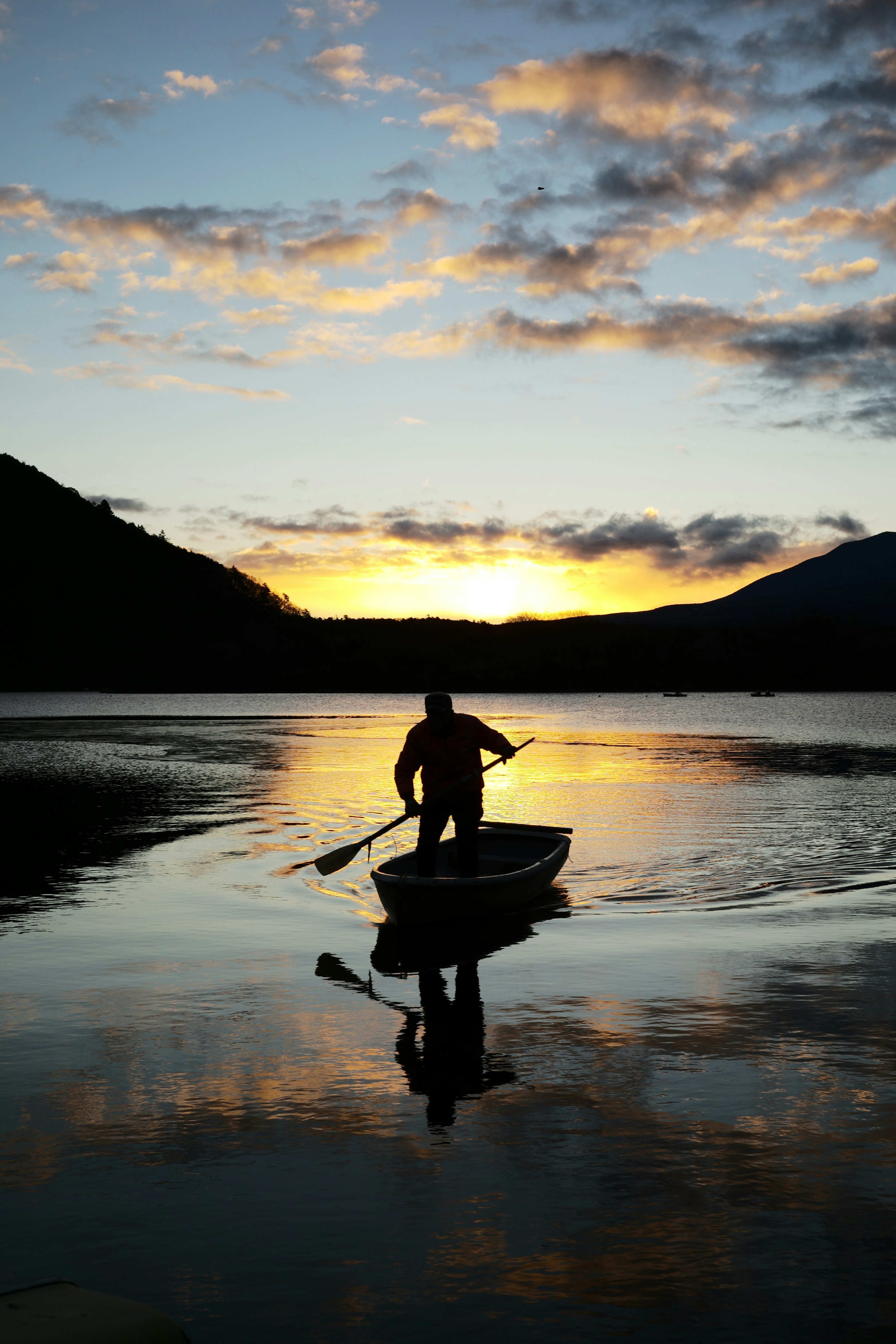 Silhouette eines Mannes, der in einem ruhigen See Boot fährt schöne Reflexion des Sonnenuntergangs