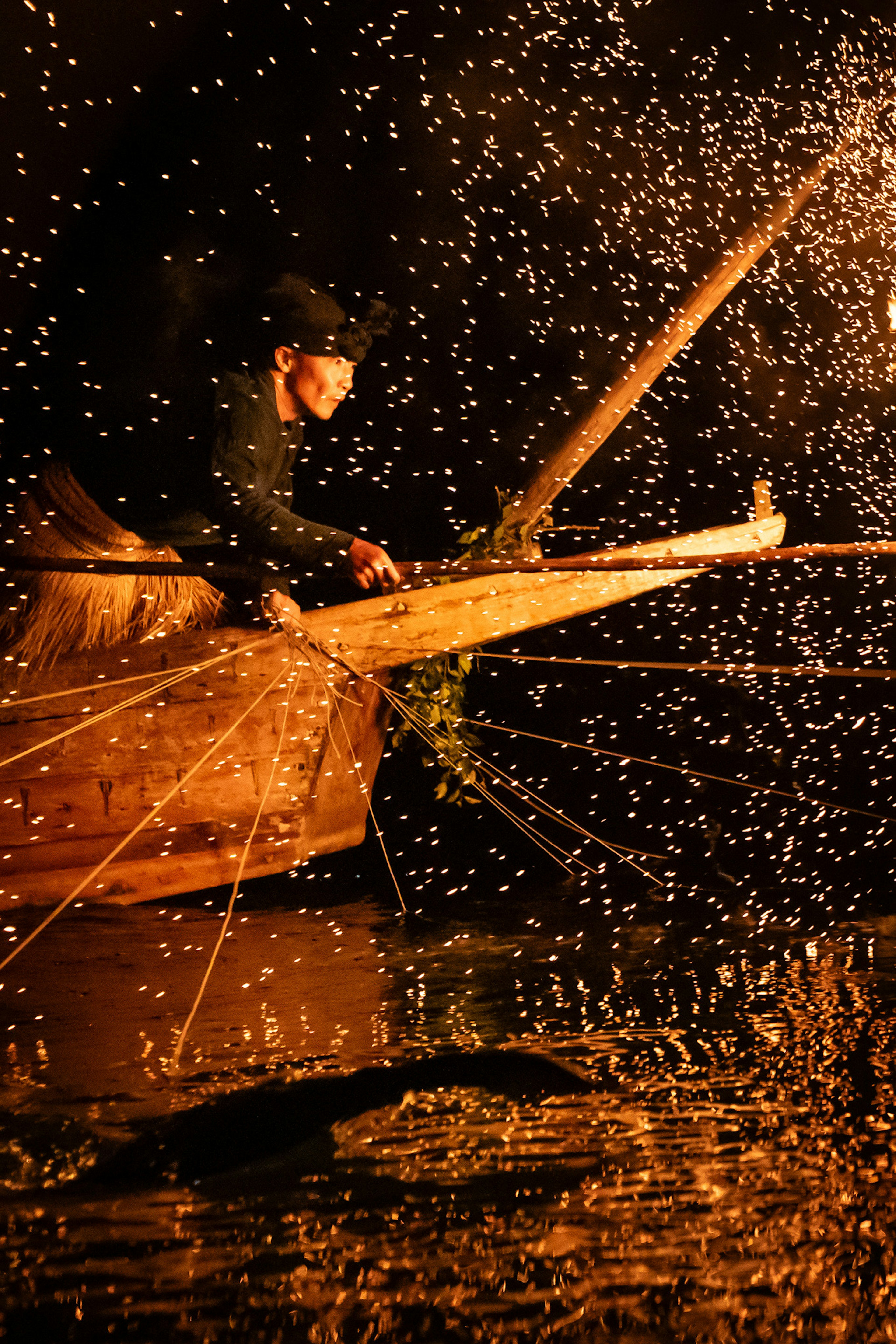 Pescatore che lavora di notte spargendo scintille sul fiume