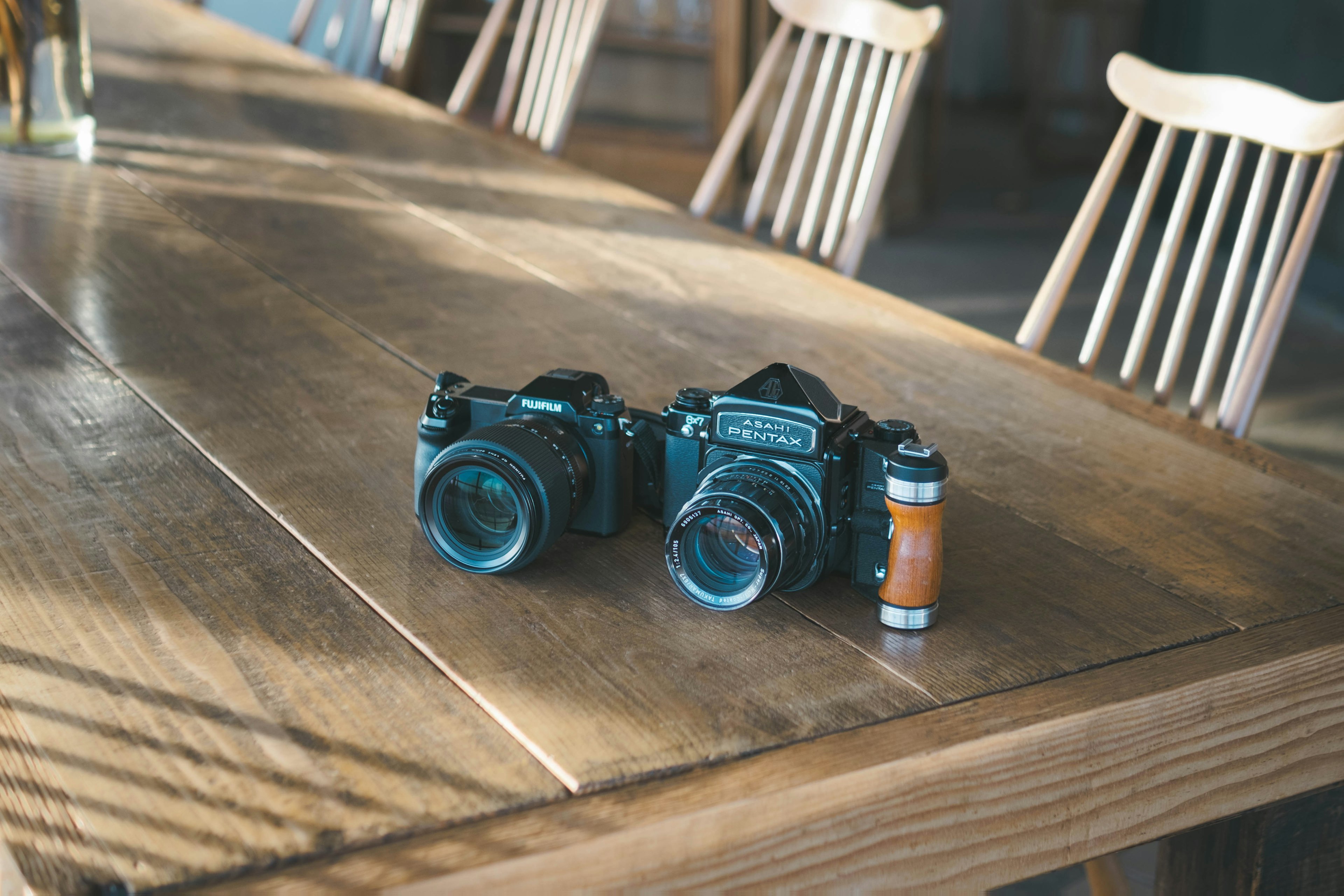 Two cameras and a roll of film on a wooden table