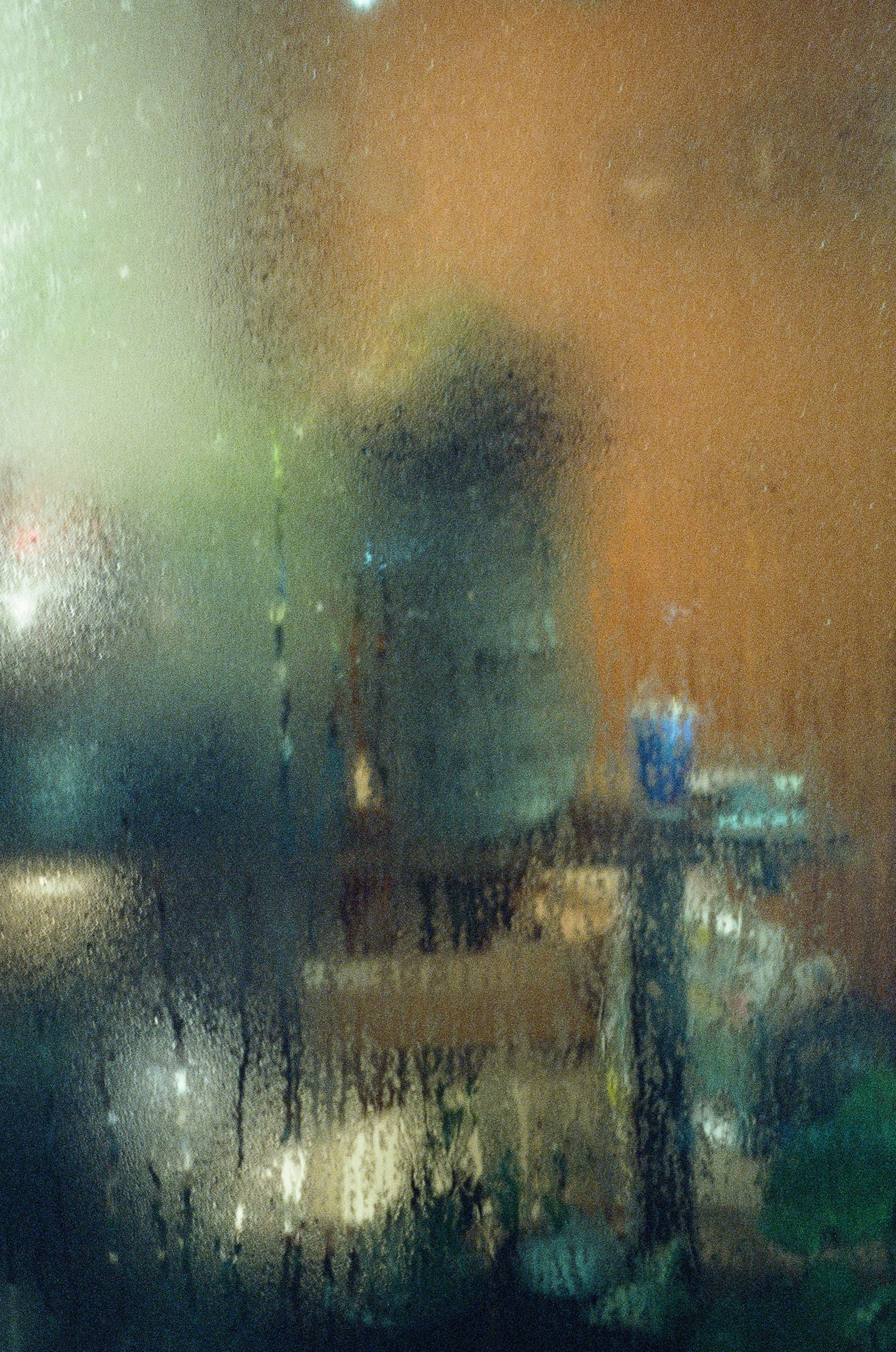 A blurred view of a cityscape through a foggy window with a faint silhouette of a person