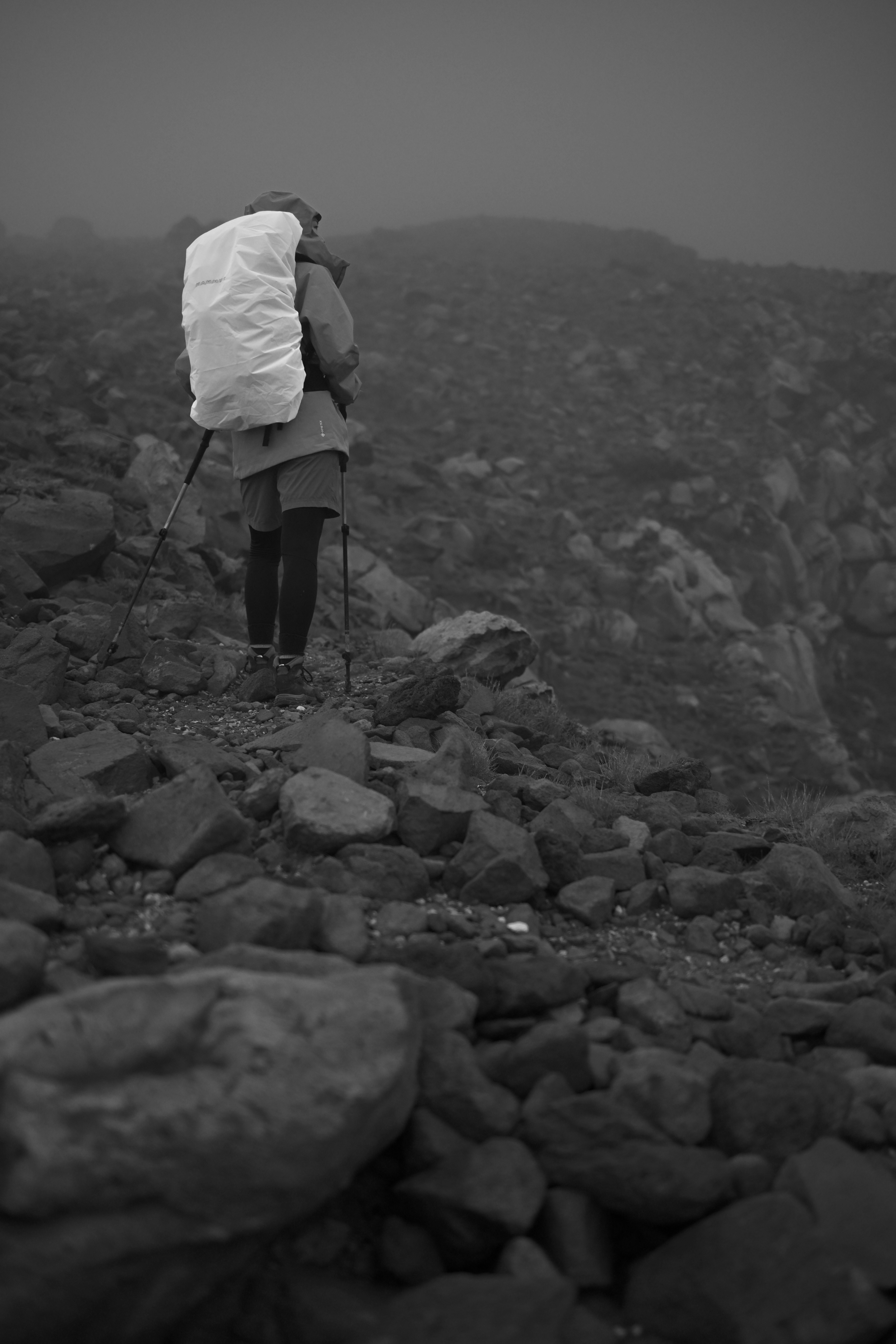 霧の中で石の道を歩く登山者のモノクロ画像