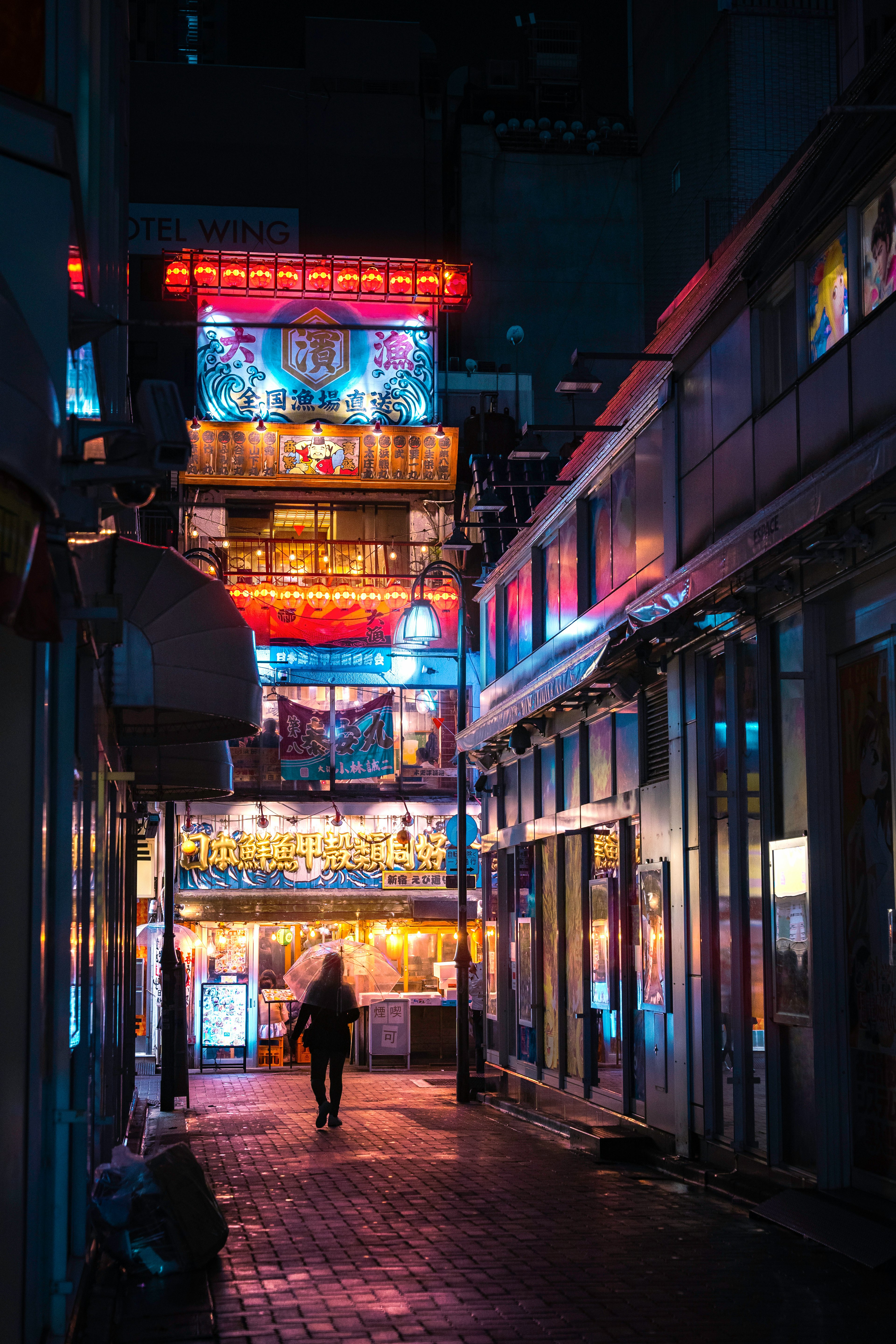 A narrow street illuminated by neon lights at night with a person walking