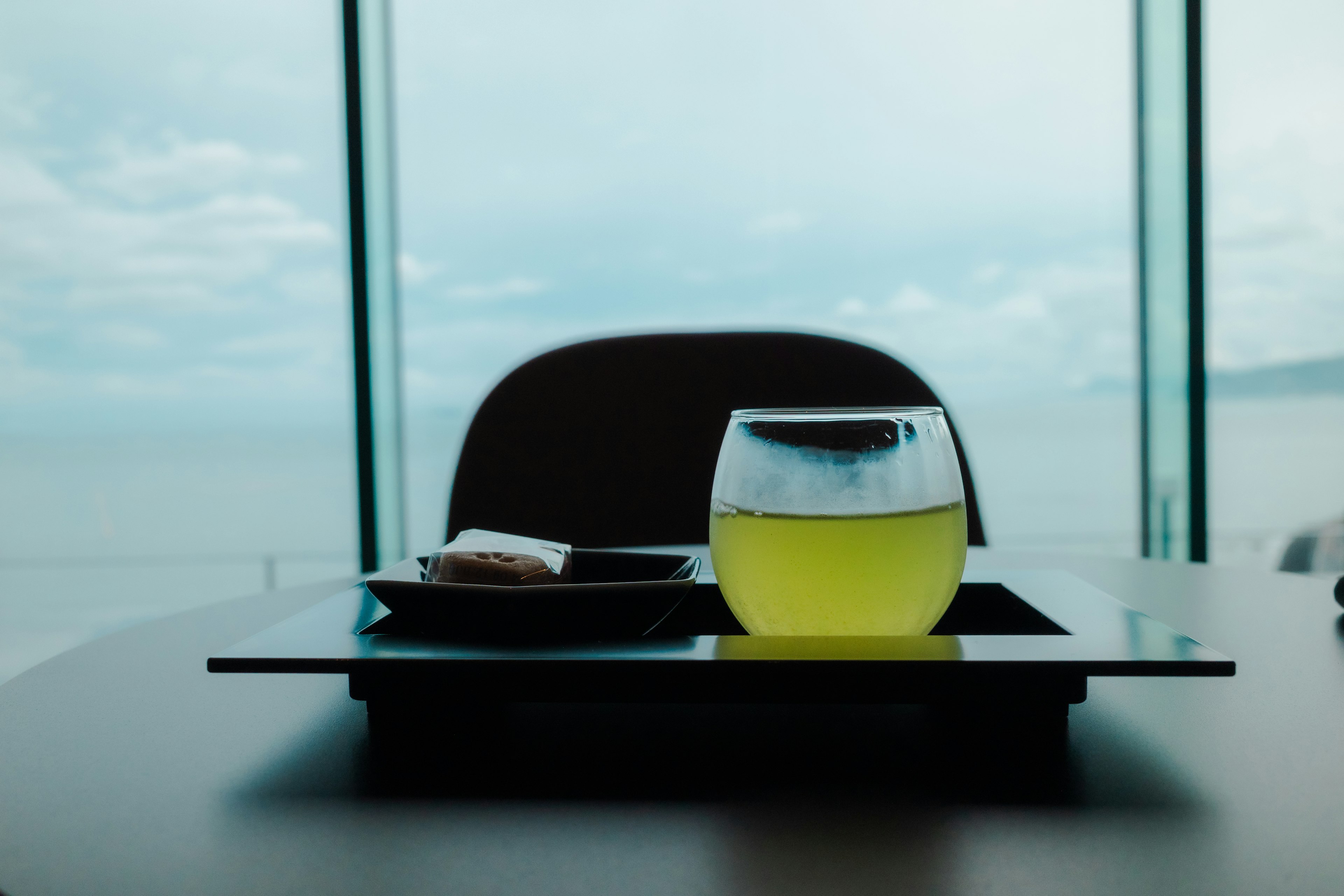 A photo of a yellow drink and a plate of snacks on a glass table