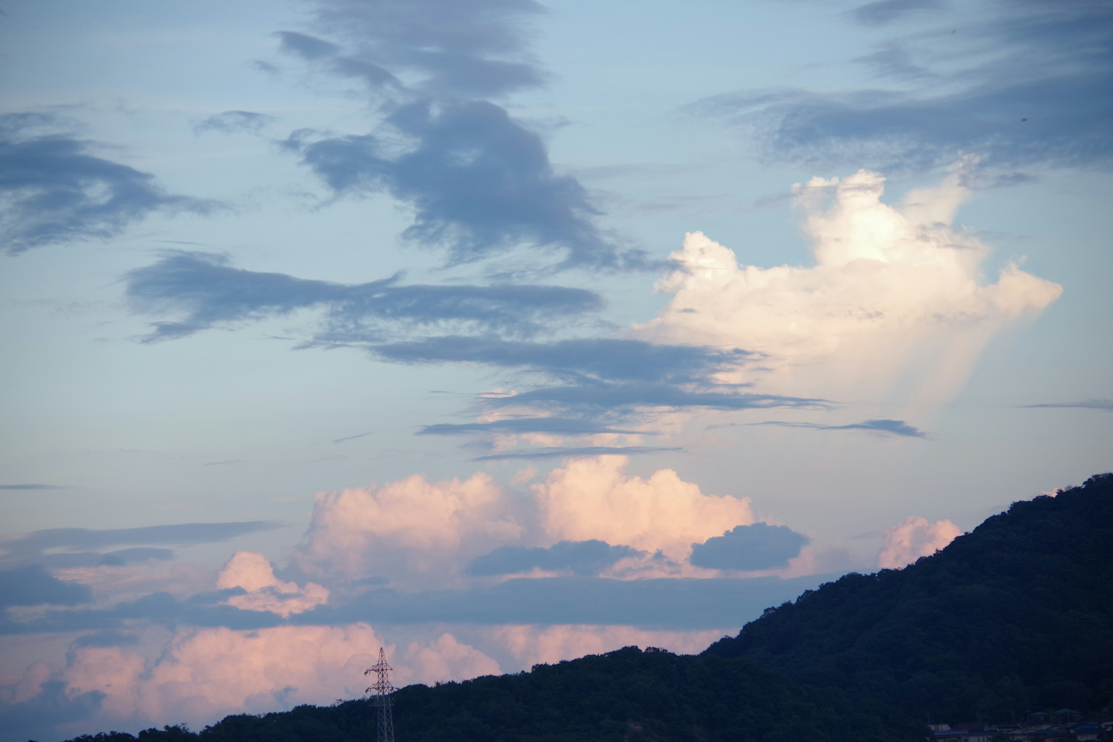 Pemandangan pegunungan dengan awan awan merah muda lembut di langit biru