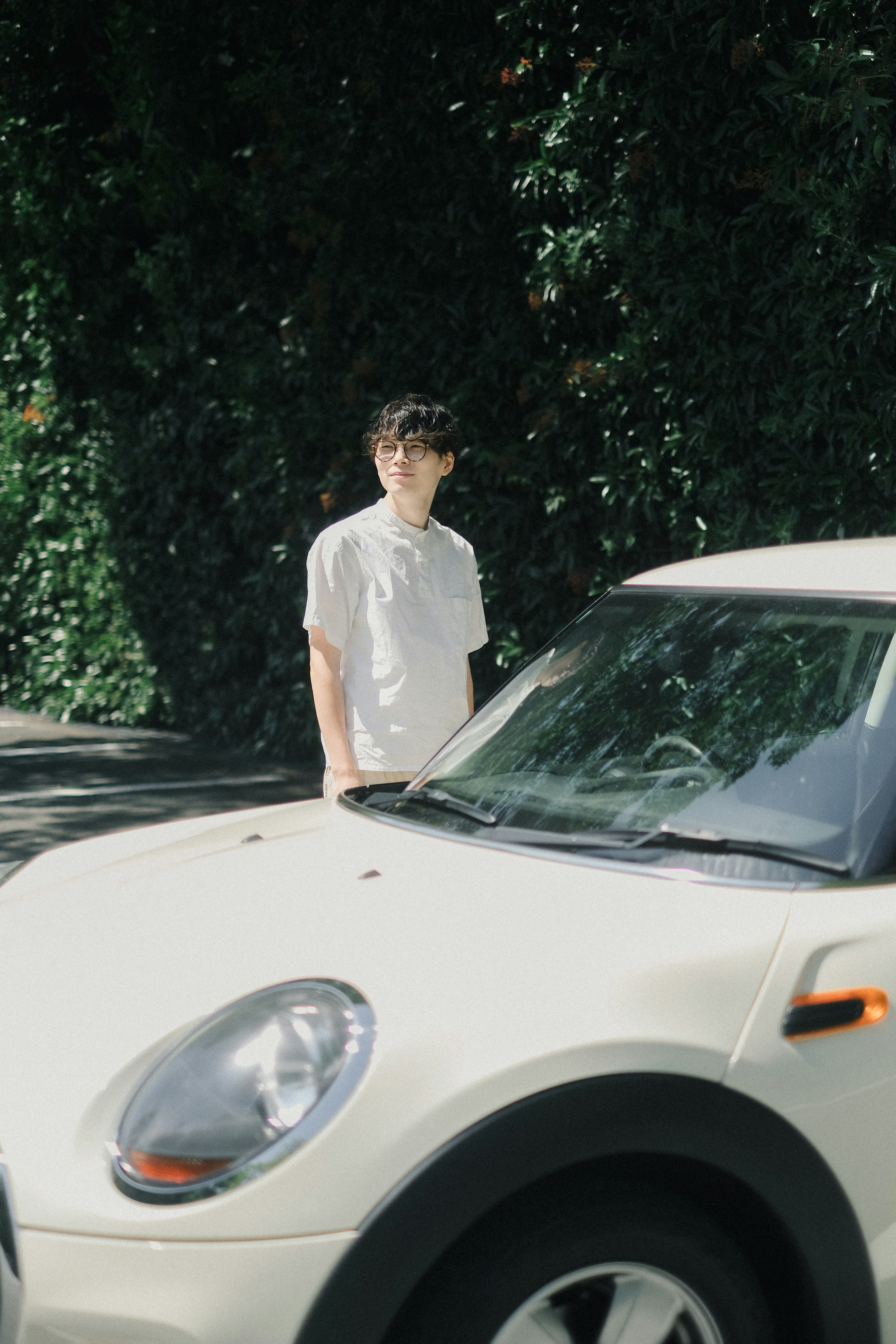 A man standing in front of a white car with green foliage in the background