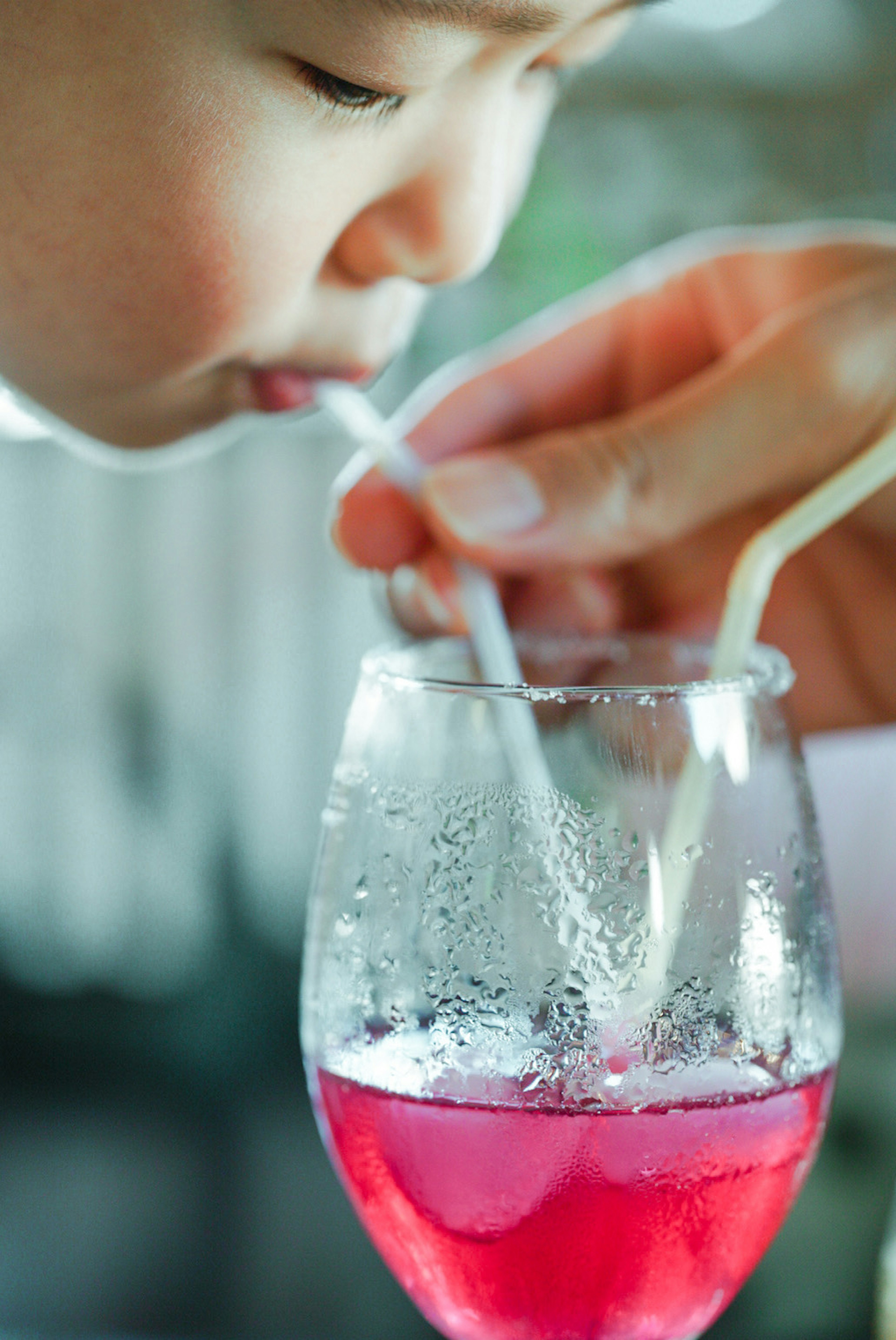 子供がストローで飲み物を飲んでいる様子 手がストローを持っている グラスの中の赤い飲み物