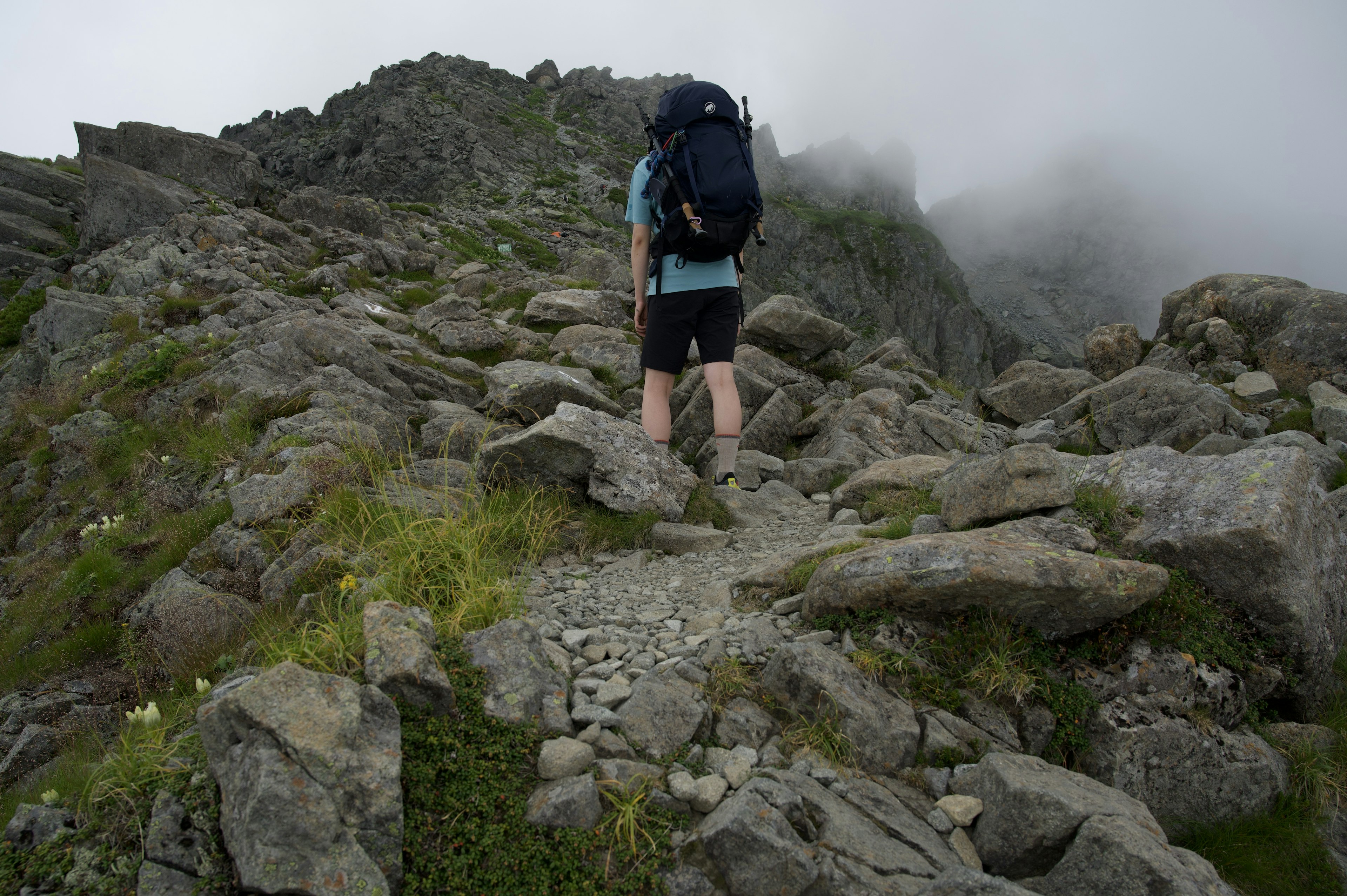 Hiker ascending a rocky mountain path shrouded in mist