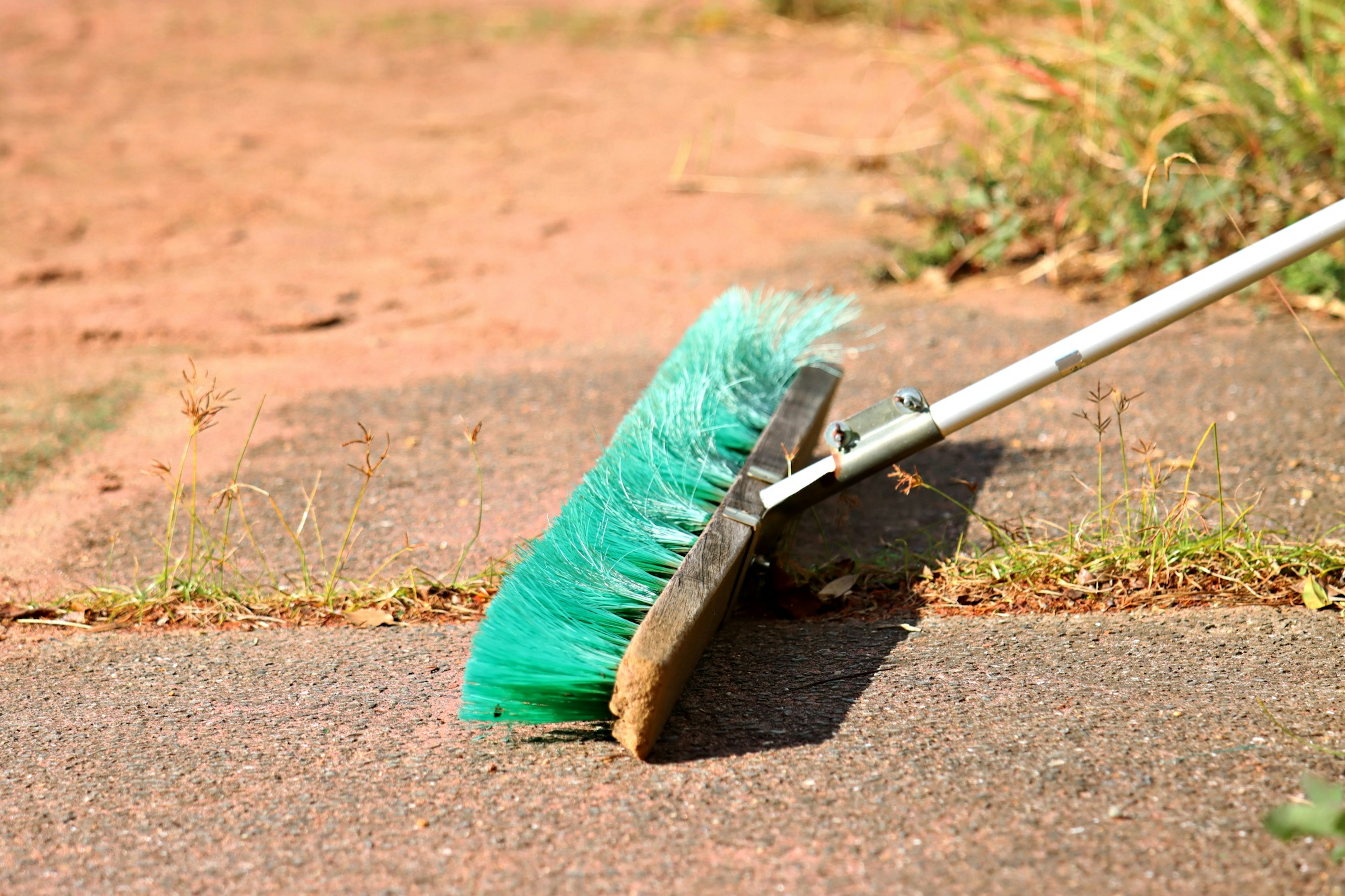 A green broom sweeping a dirt path