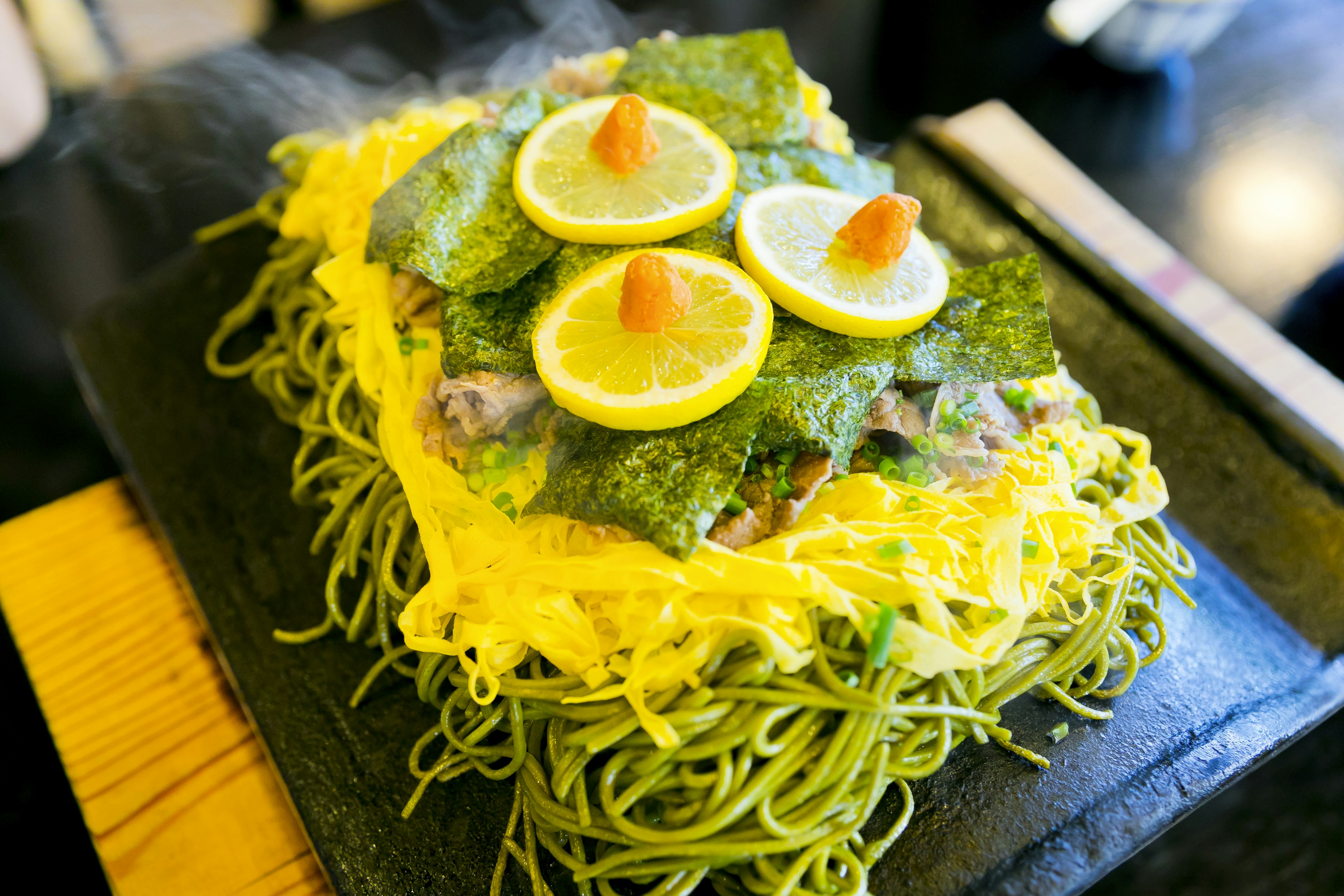 Plato con fideos verdes cubiertos de huevo y rodajas de limón