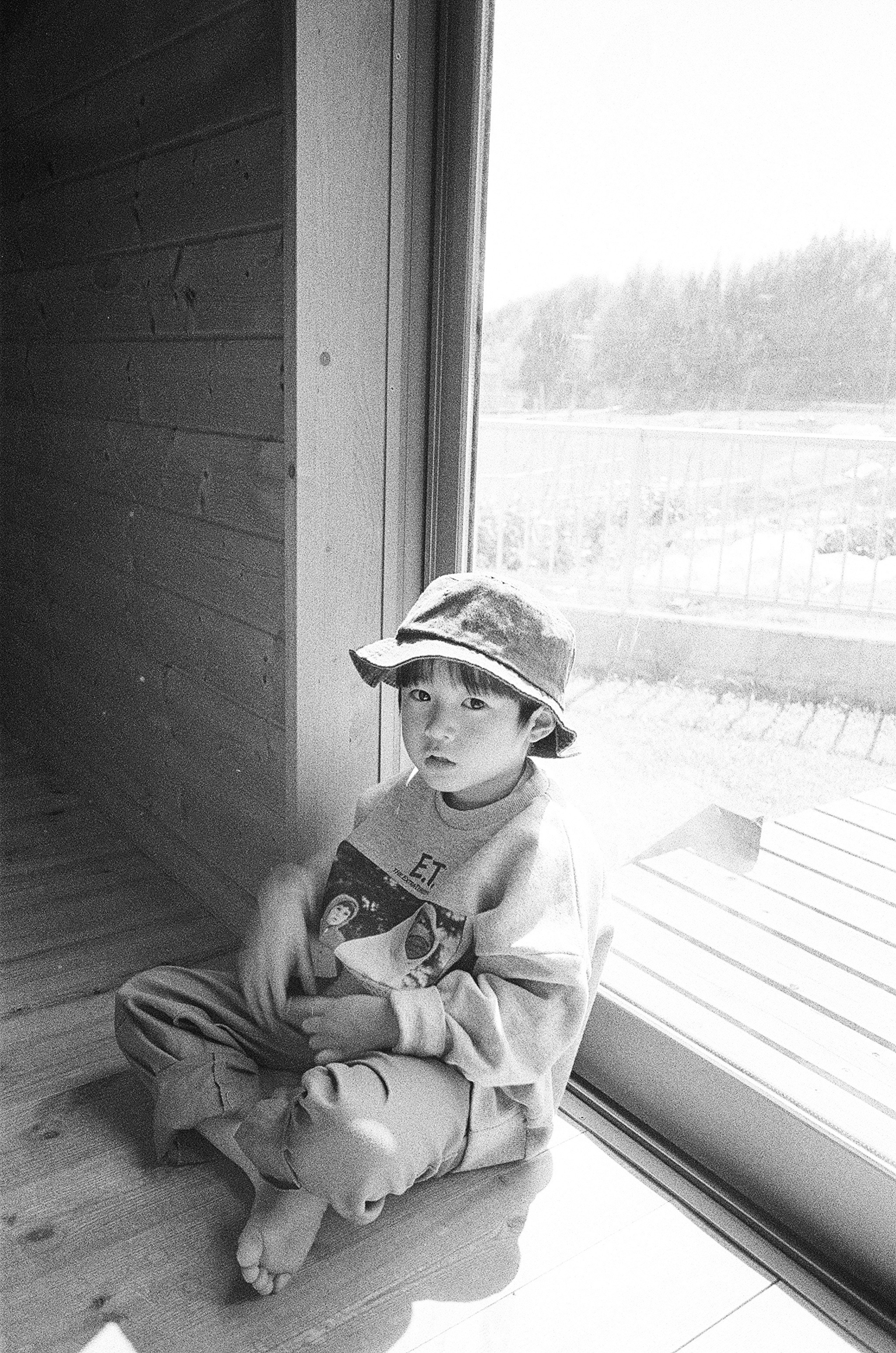 A boy sitting by the window wearing a hat with a thoughtful expression