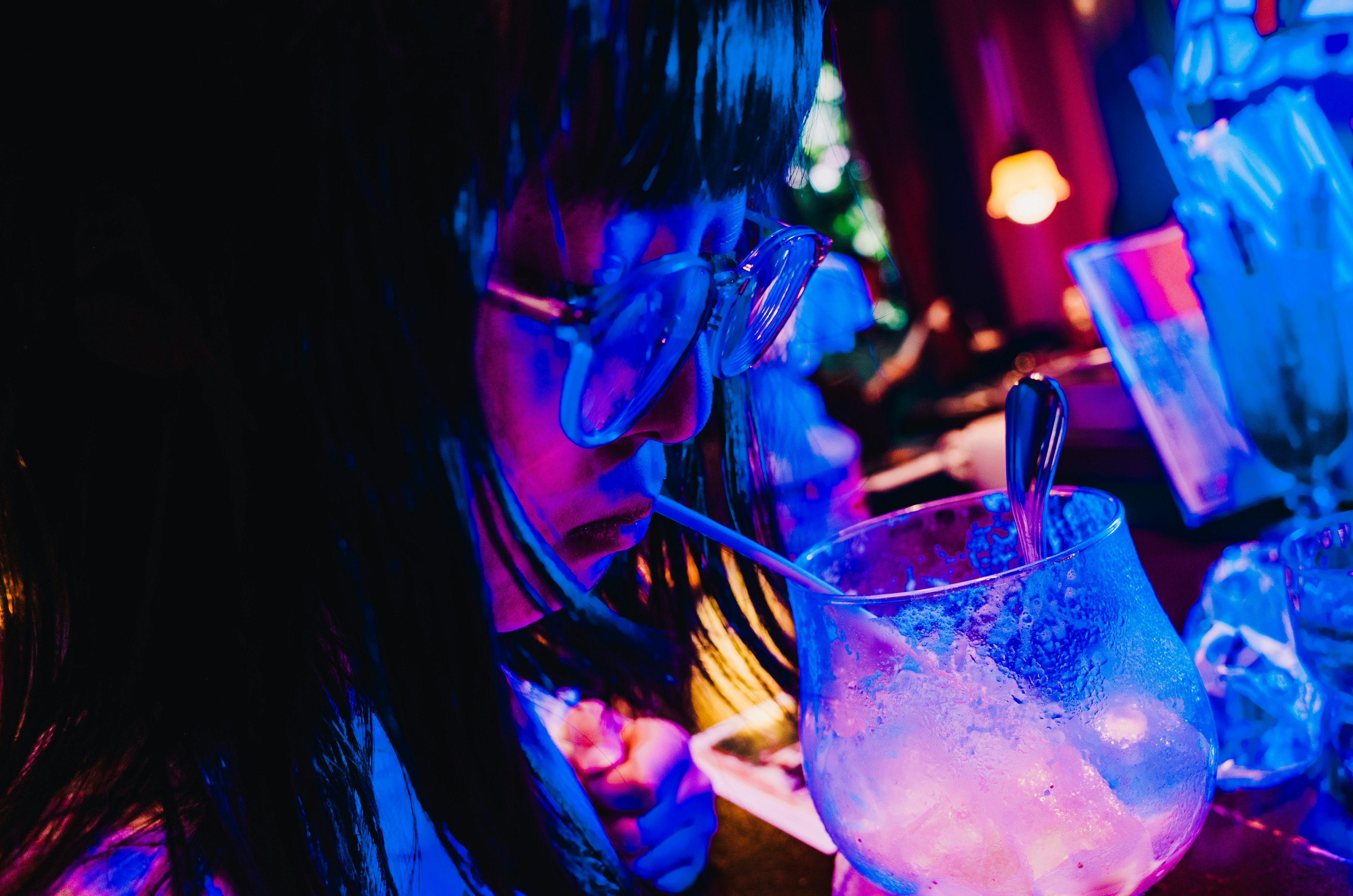 A woman sipping a colorful drink under vibrant lighting