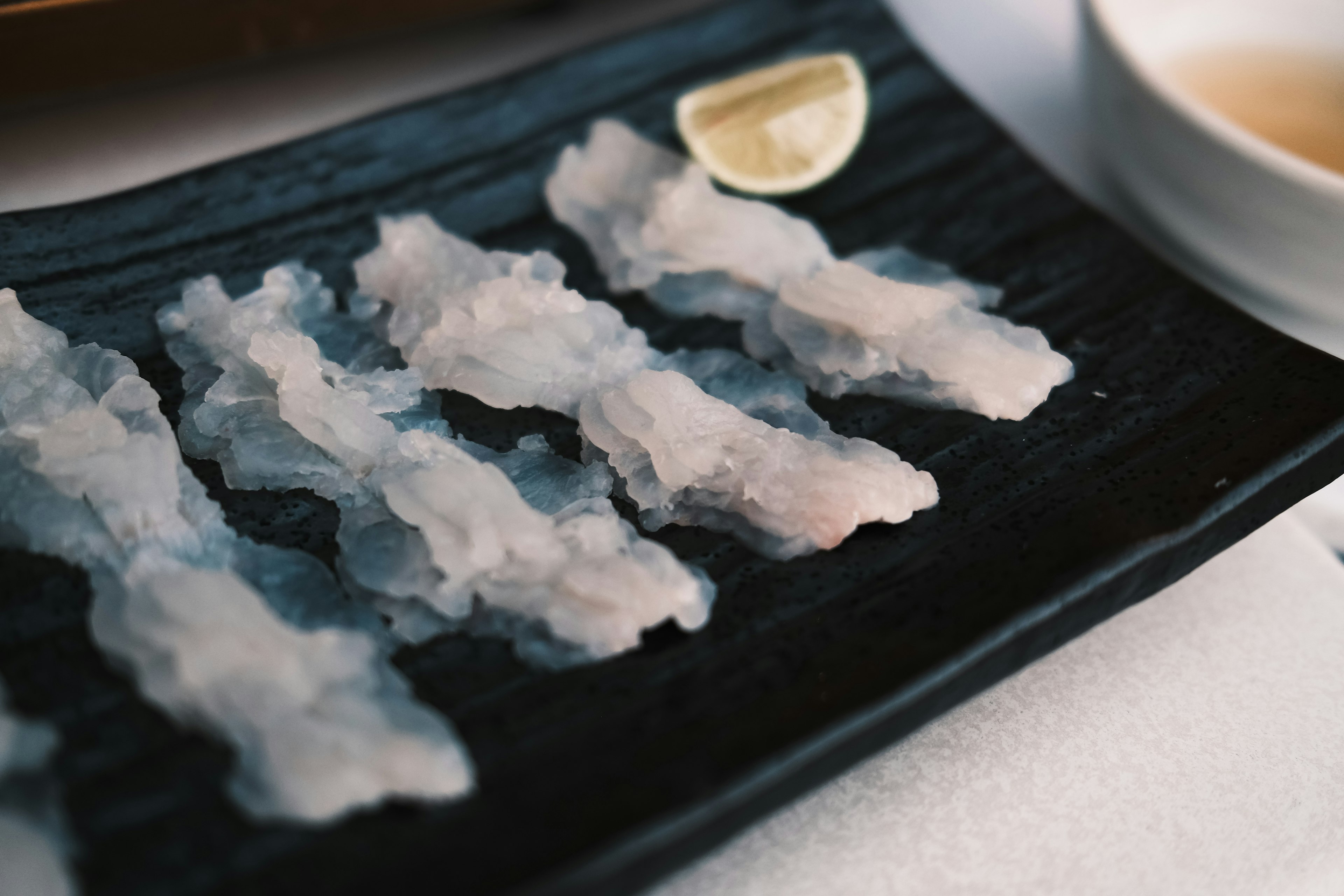 Sashimi segar yang disusun di atas piring hitam dengan seiris lemon