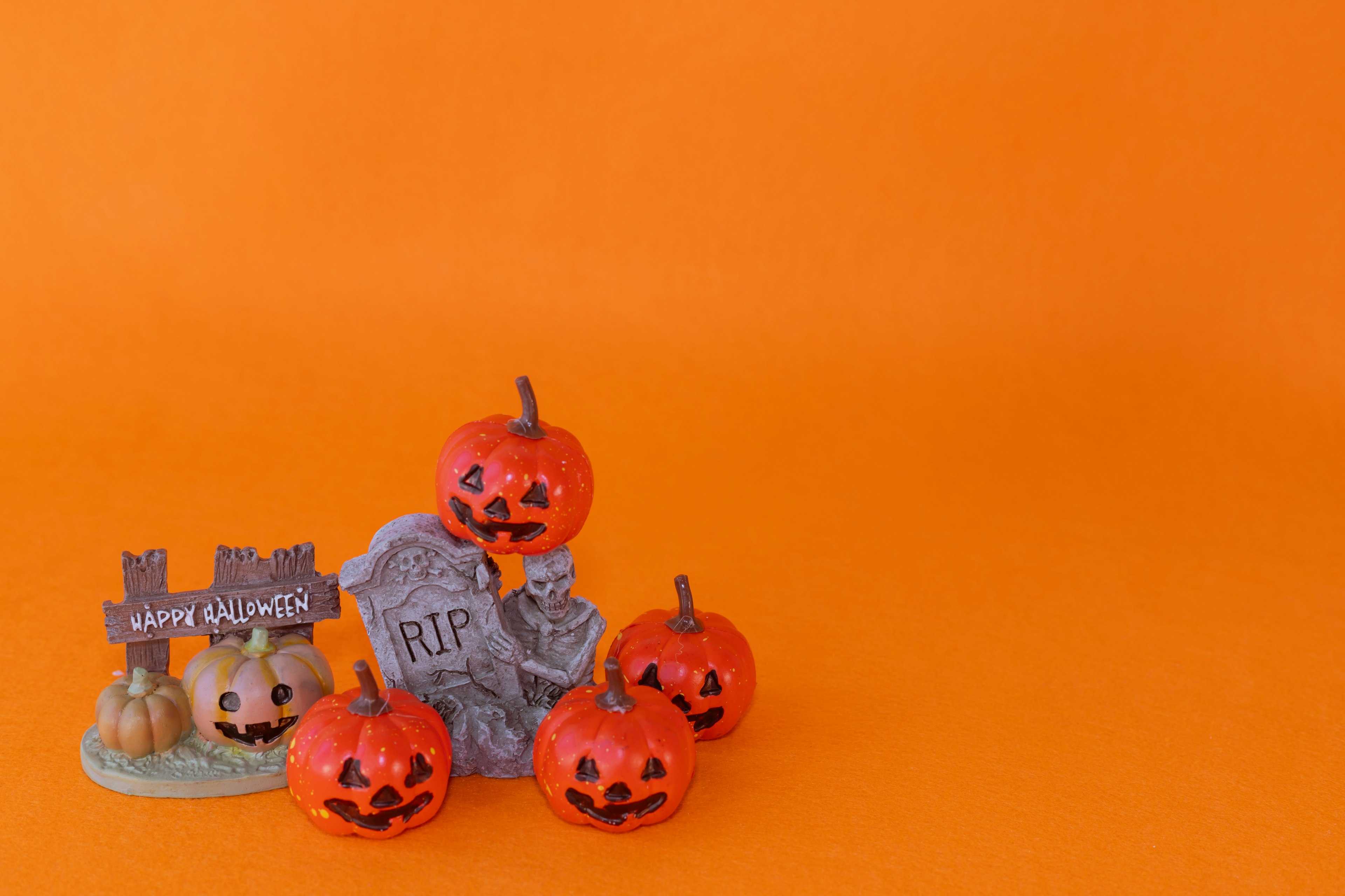 Five jack-o'-lanterns and a tombstone decoration on an orange background