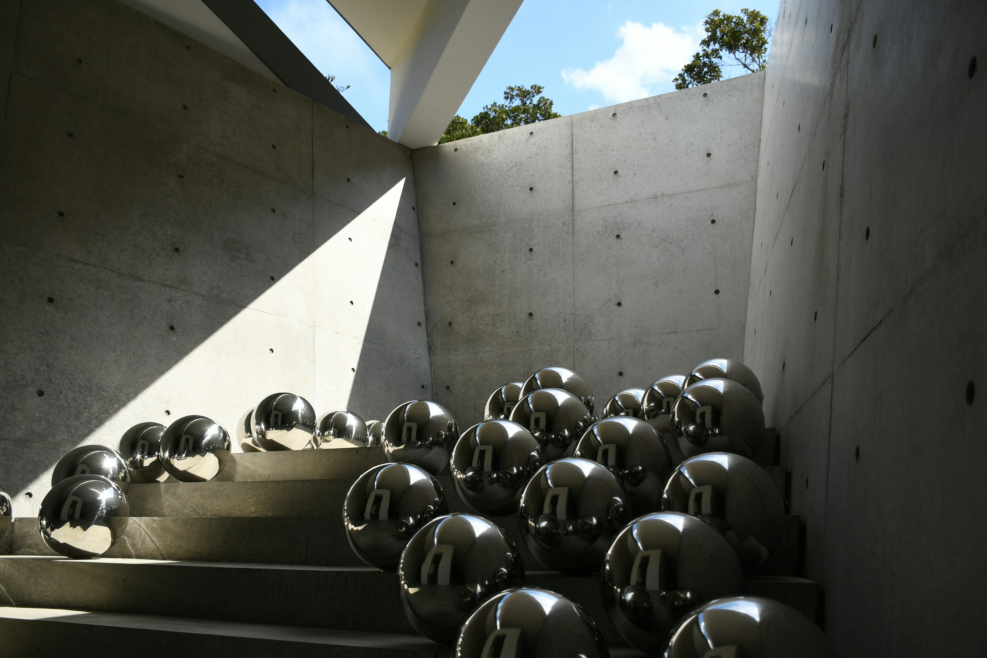 Installation artistique contemporaine avec des murs en béton et des sphères argentées disposées sur des marches