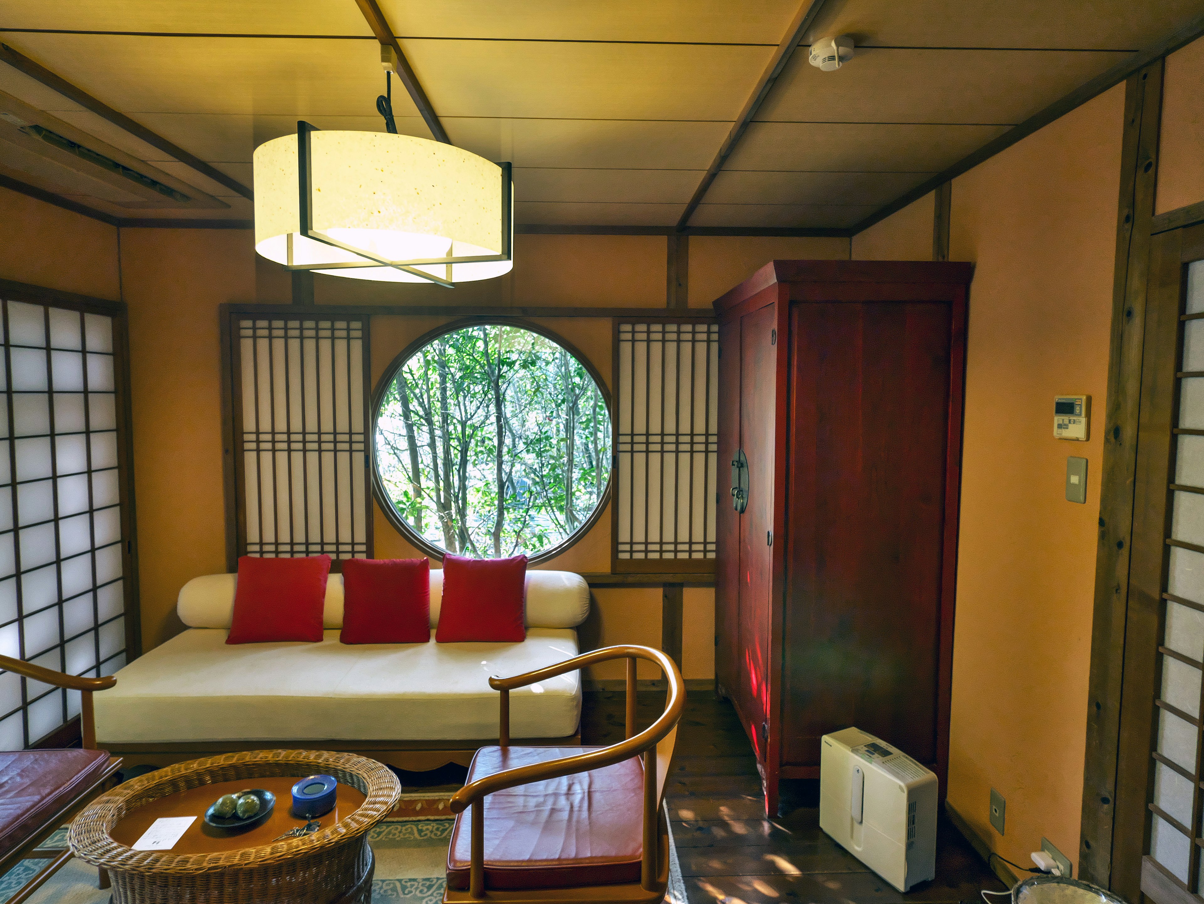 A Japanese-style interior featuring a round window a living space with a sofa adorned with red cushions and wooden furniture