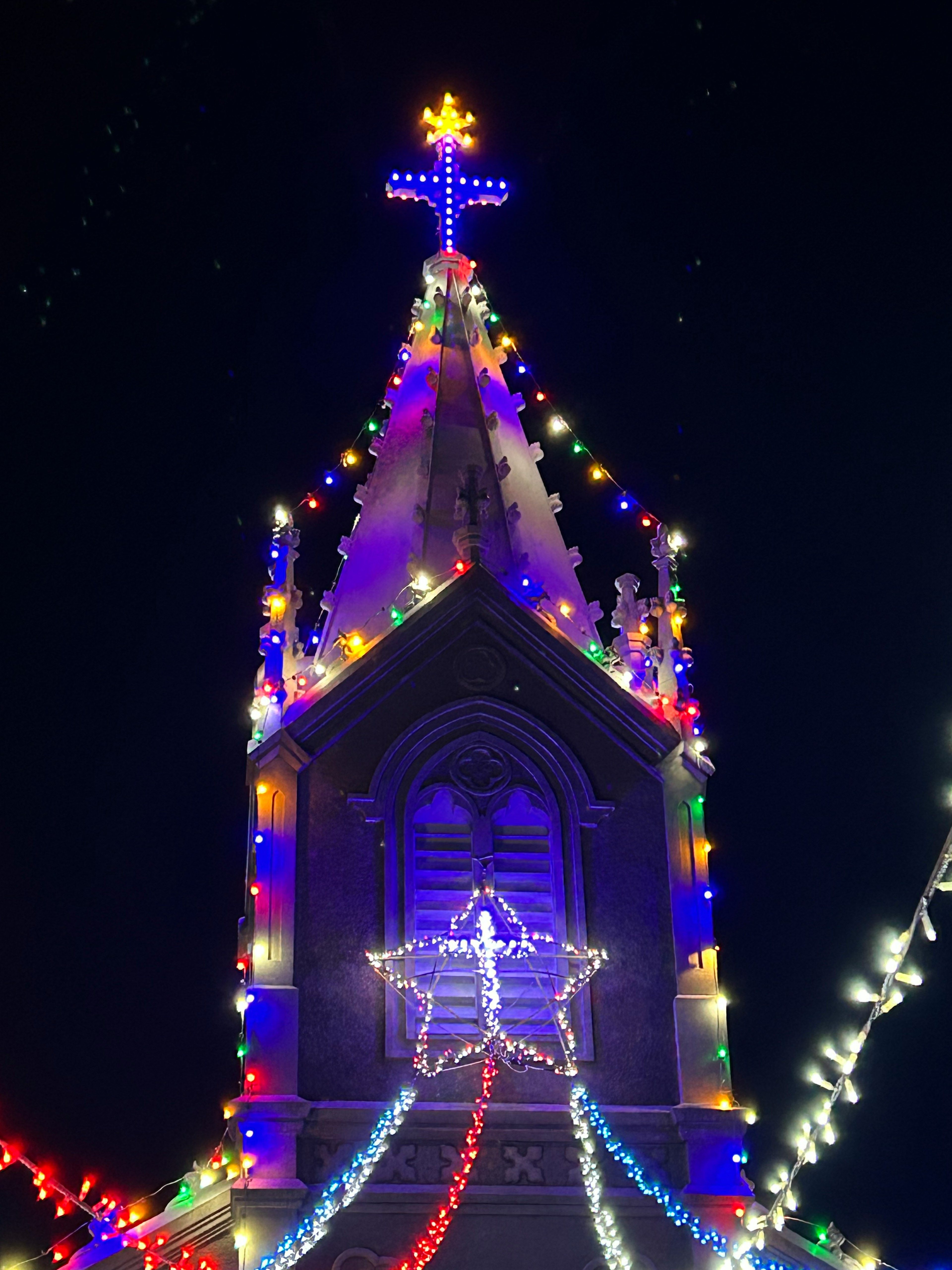 Kirchturm mit bunten Weihnachtslichtern unter einem Nachthimmel geschmückt