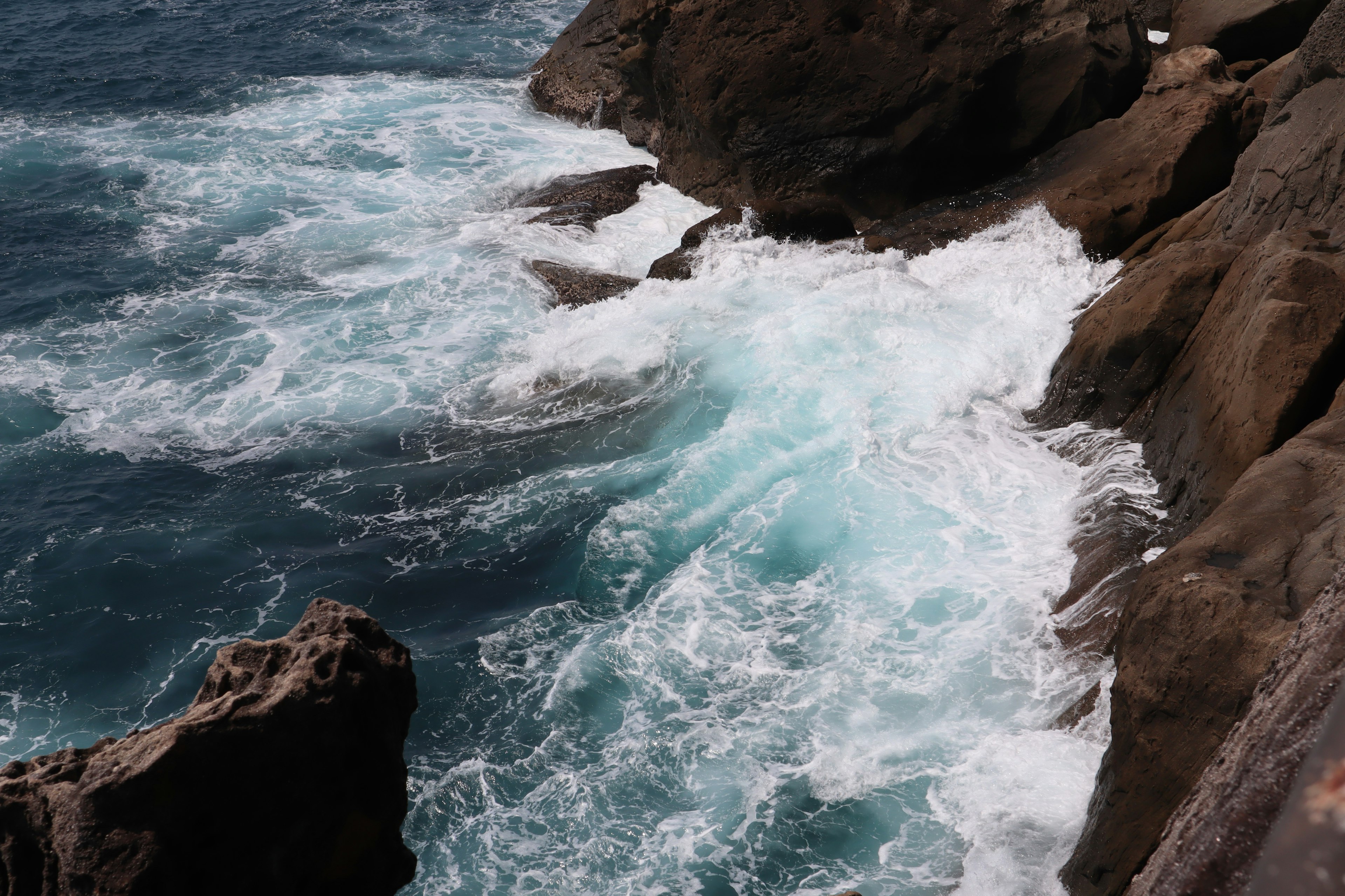 Waves crashing against rocky shore with blue ocean