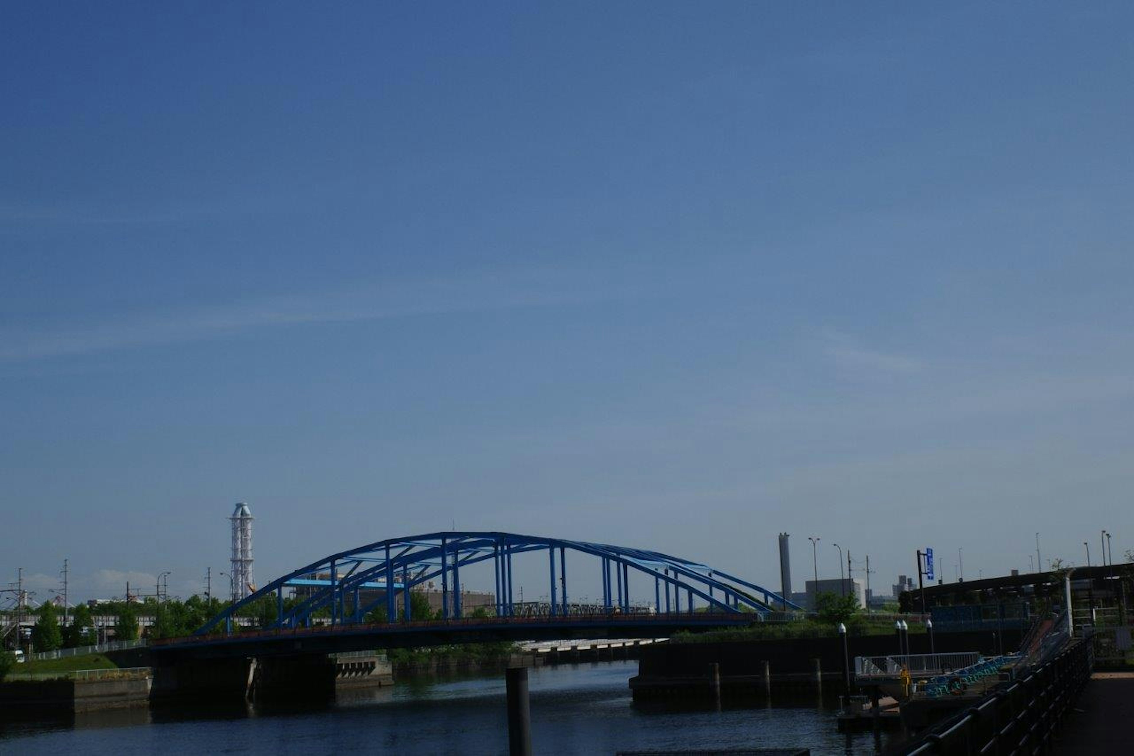 Un pont bleu s'étend sur une rivière calme sous un ciel clair