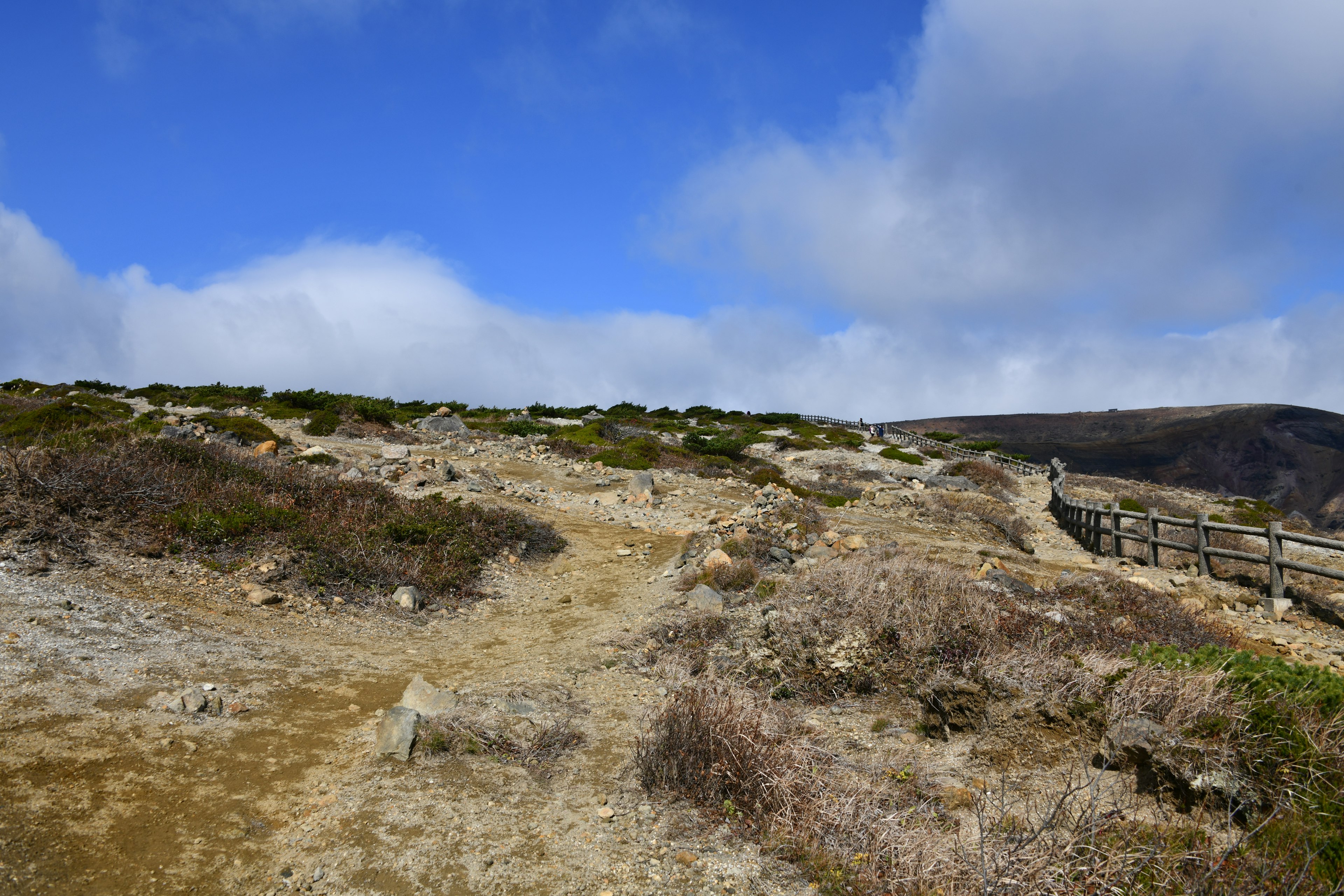 Un paysage avec un terrain accidenté et un chemin sous un ciel bleu avec des nuages blancs