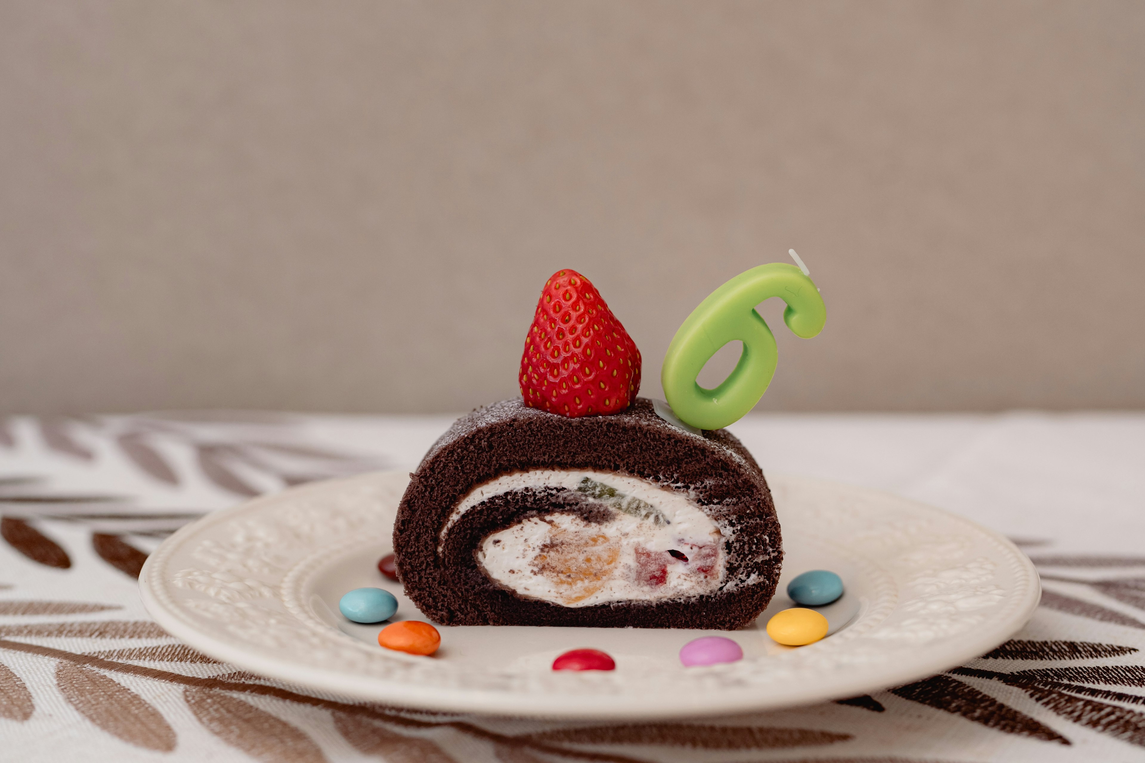 Slice of chocolate roll cake topped with a strawberry and a green candle