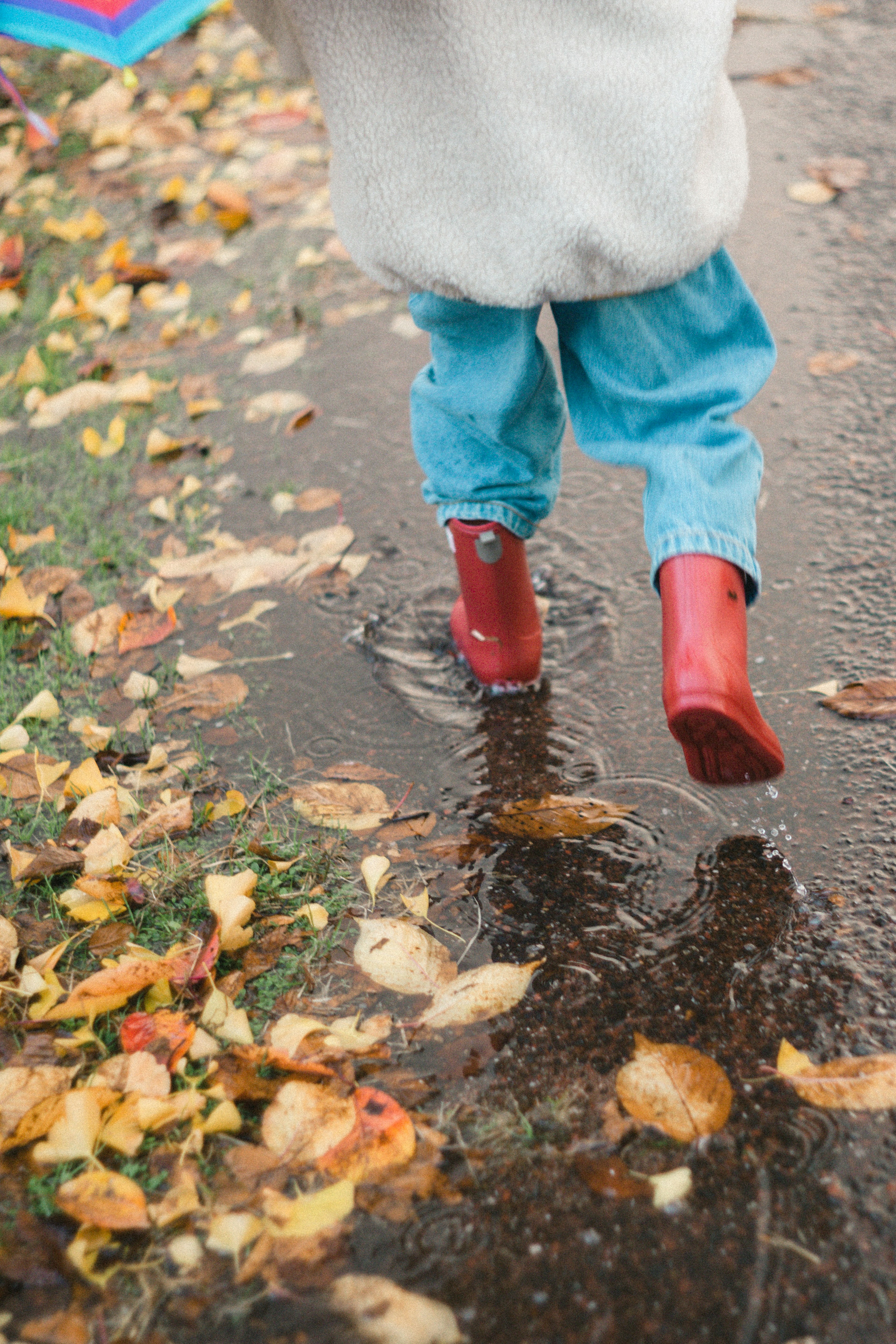 A child walking through a puddle wearing red rubber boots