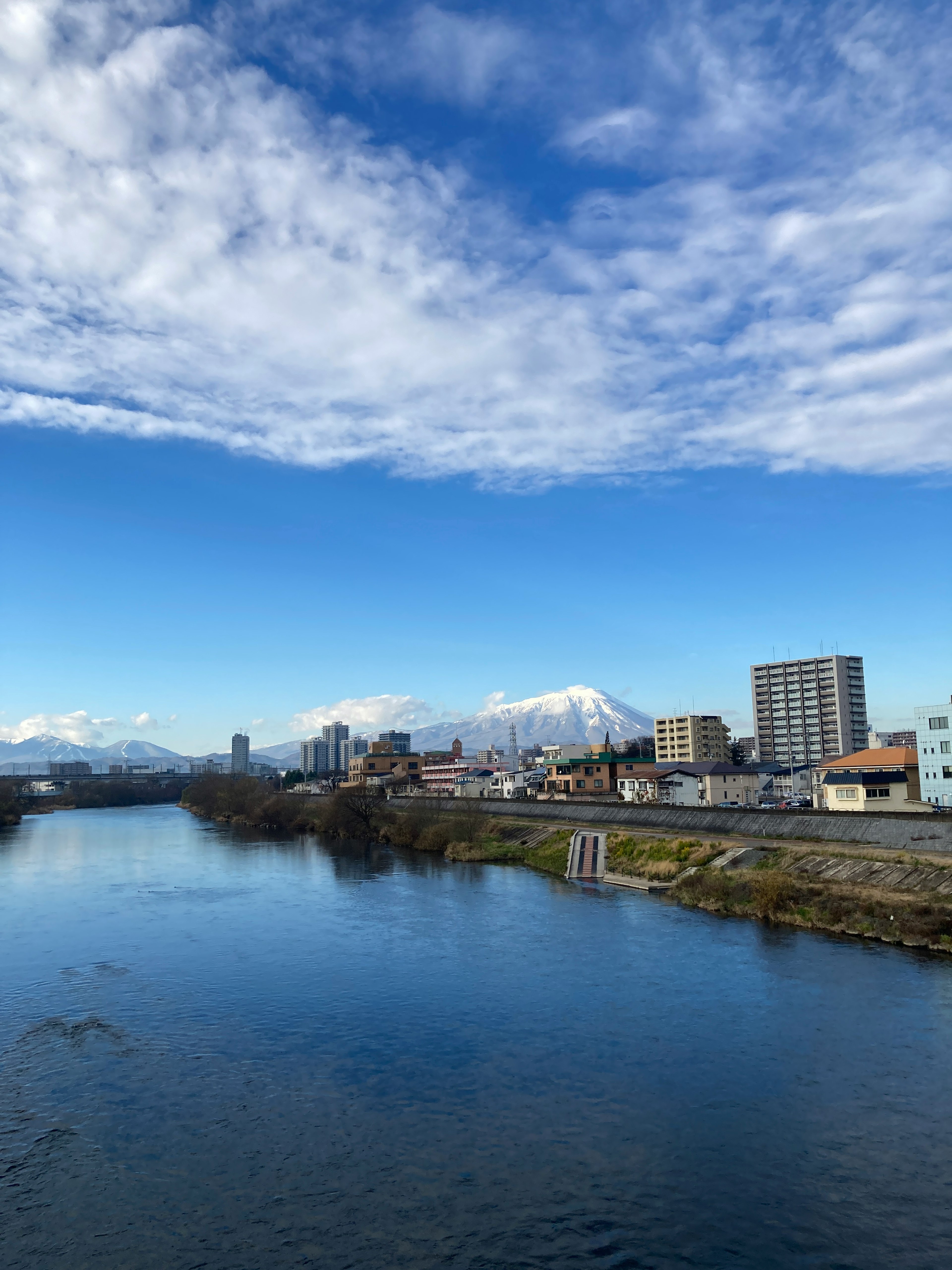 Scenic view of a river under a blue sky with distant snowy mountains and nearby buildings