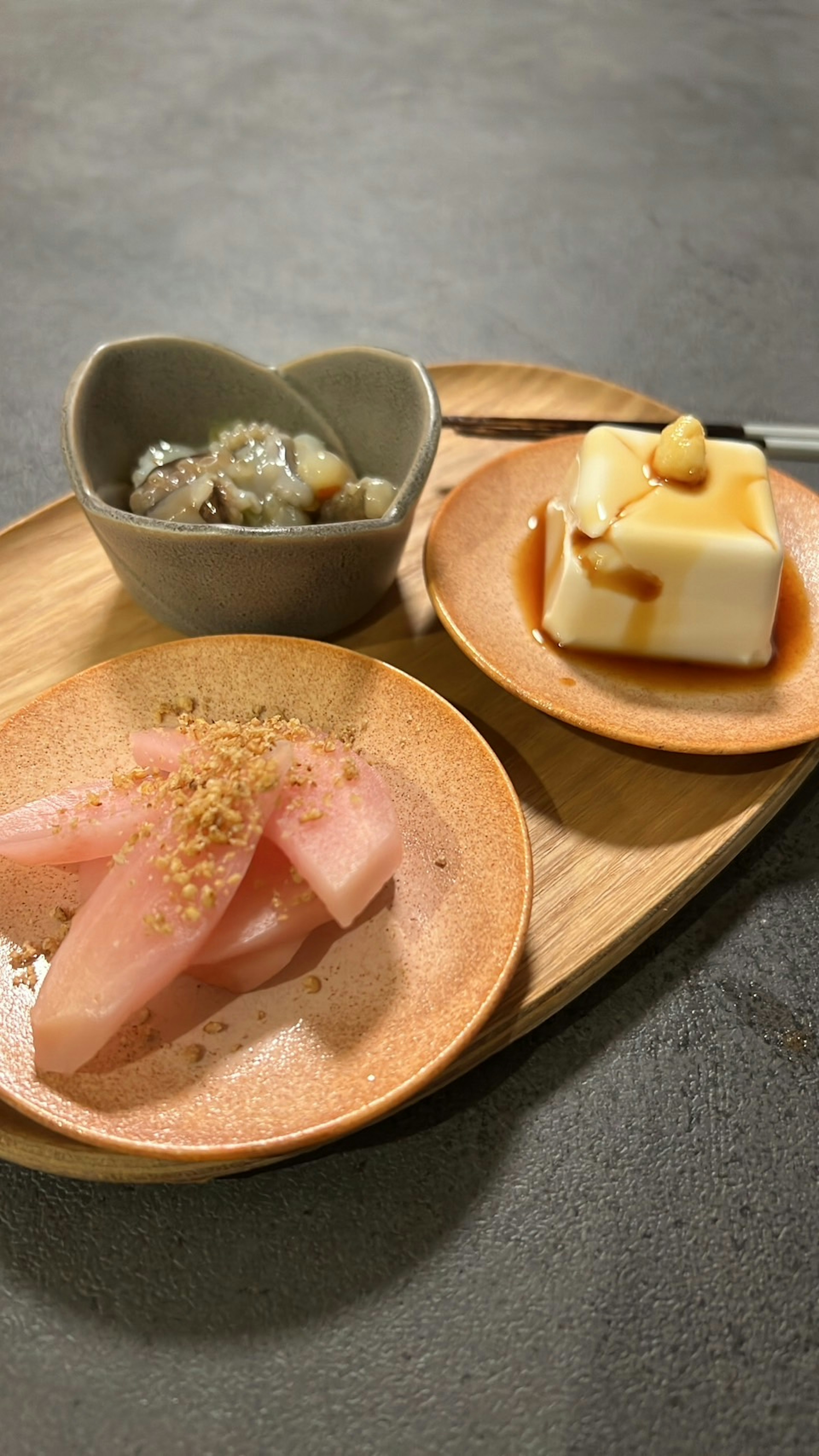 A wooden platter featuring a heart-shaped dish with traditional side dish and two plates of dessert