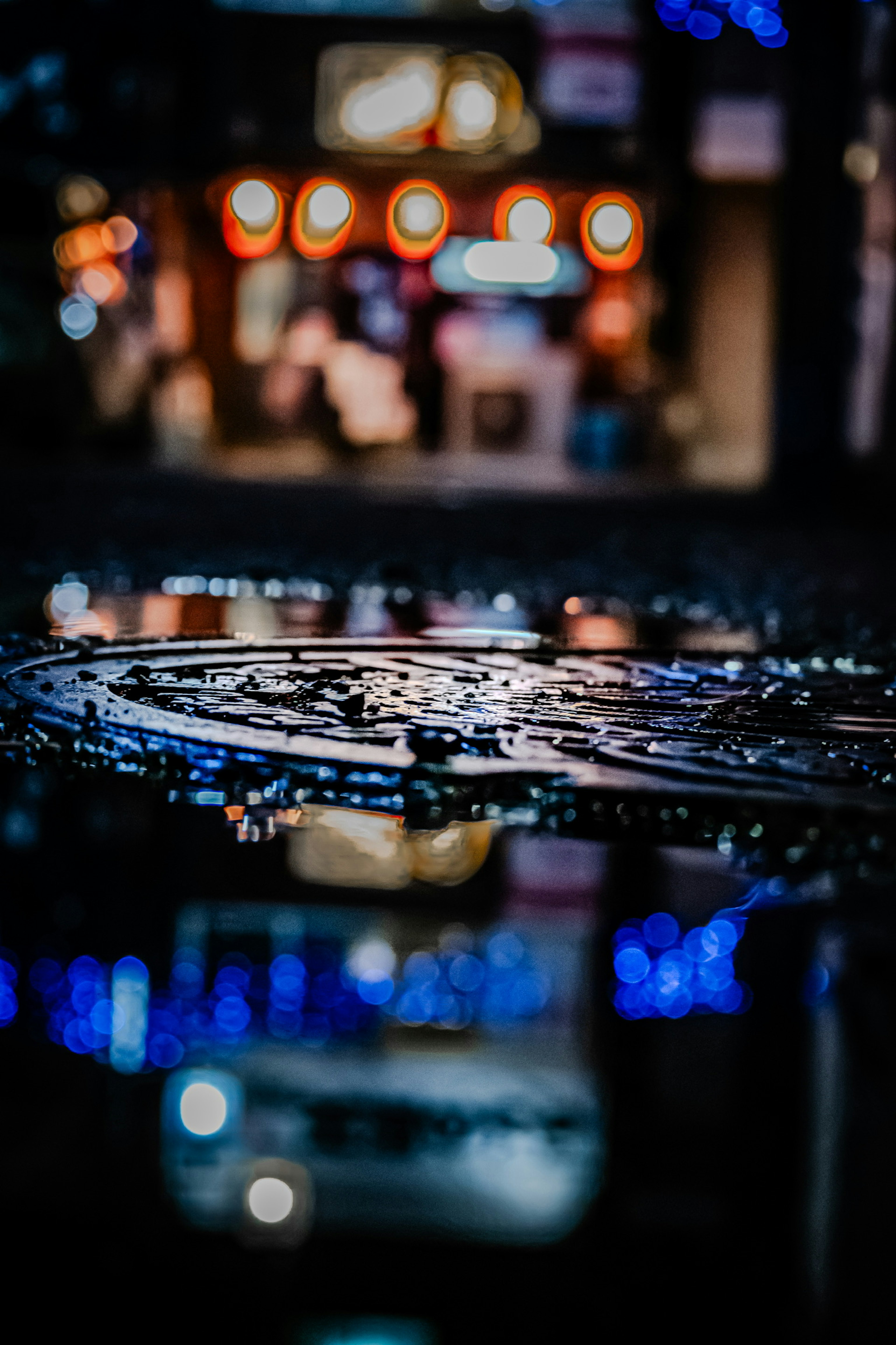 Reflections of neon lights and silhouettes of people in a rain puddle