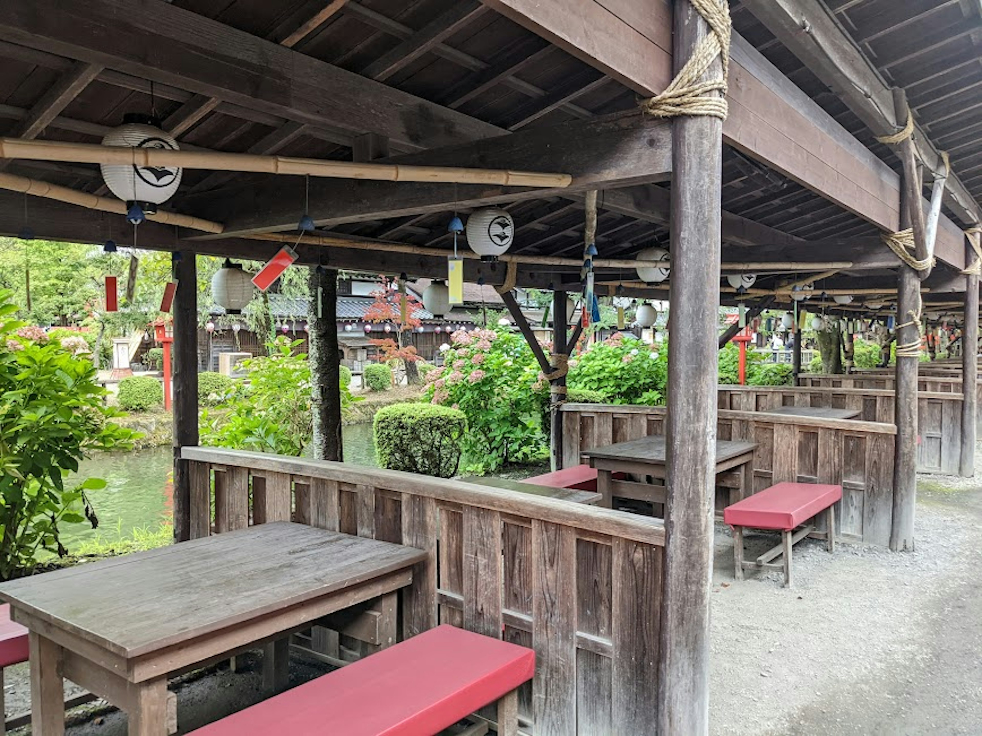 Área de comedor al aire libre tradicional japonesa con mesas de madera y bancos rojos rodeados de vegetación