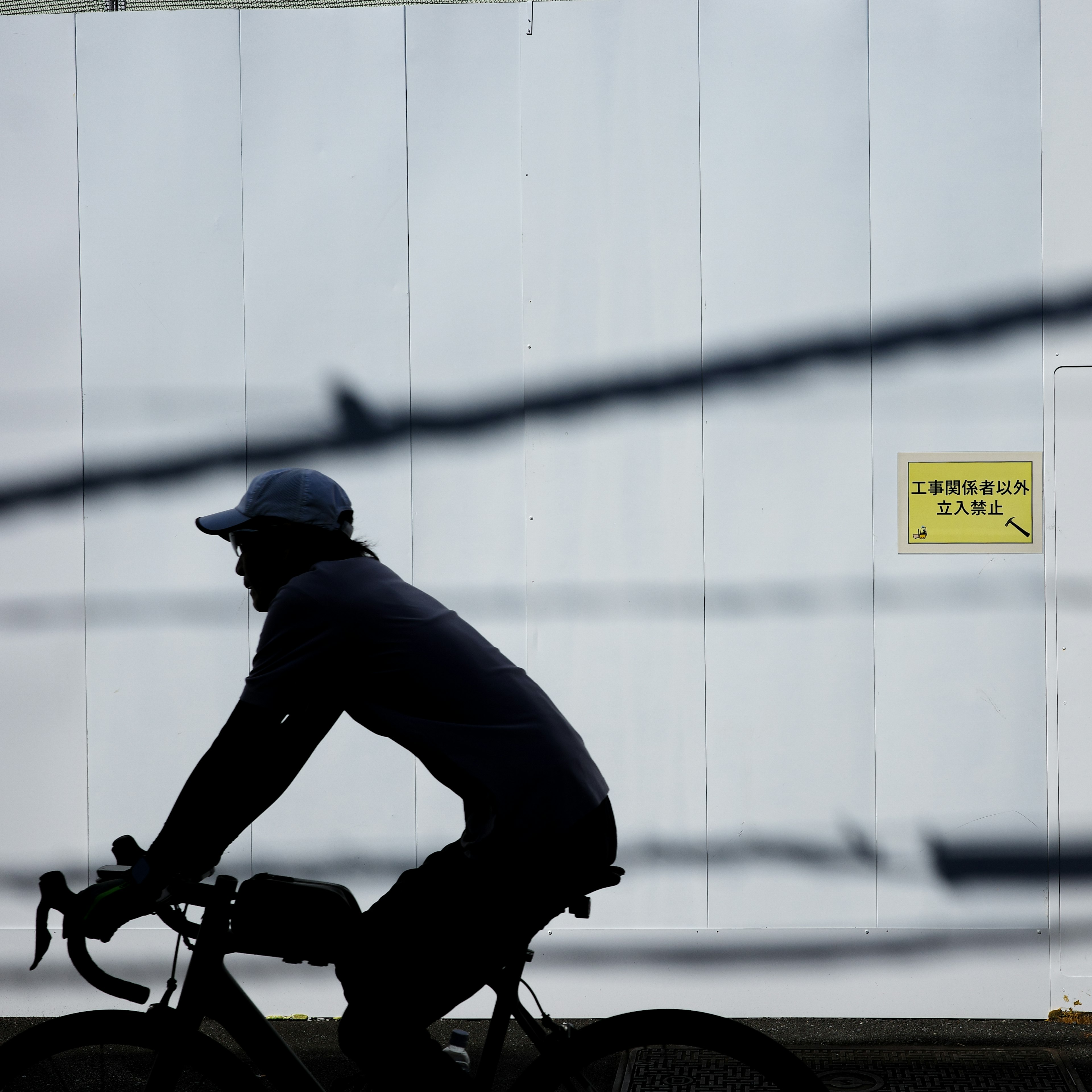 Silhouette eines Mannes, der auf einem Fahrrad gegen eine weiße Wand fährt