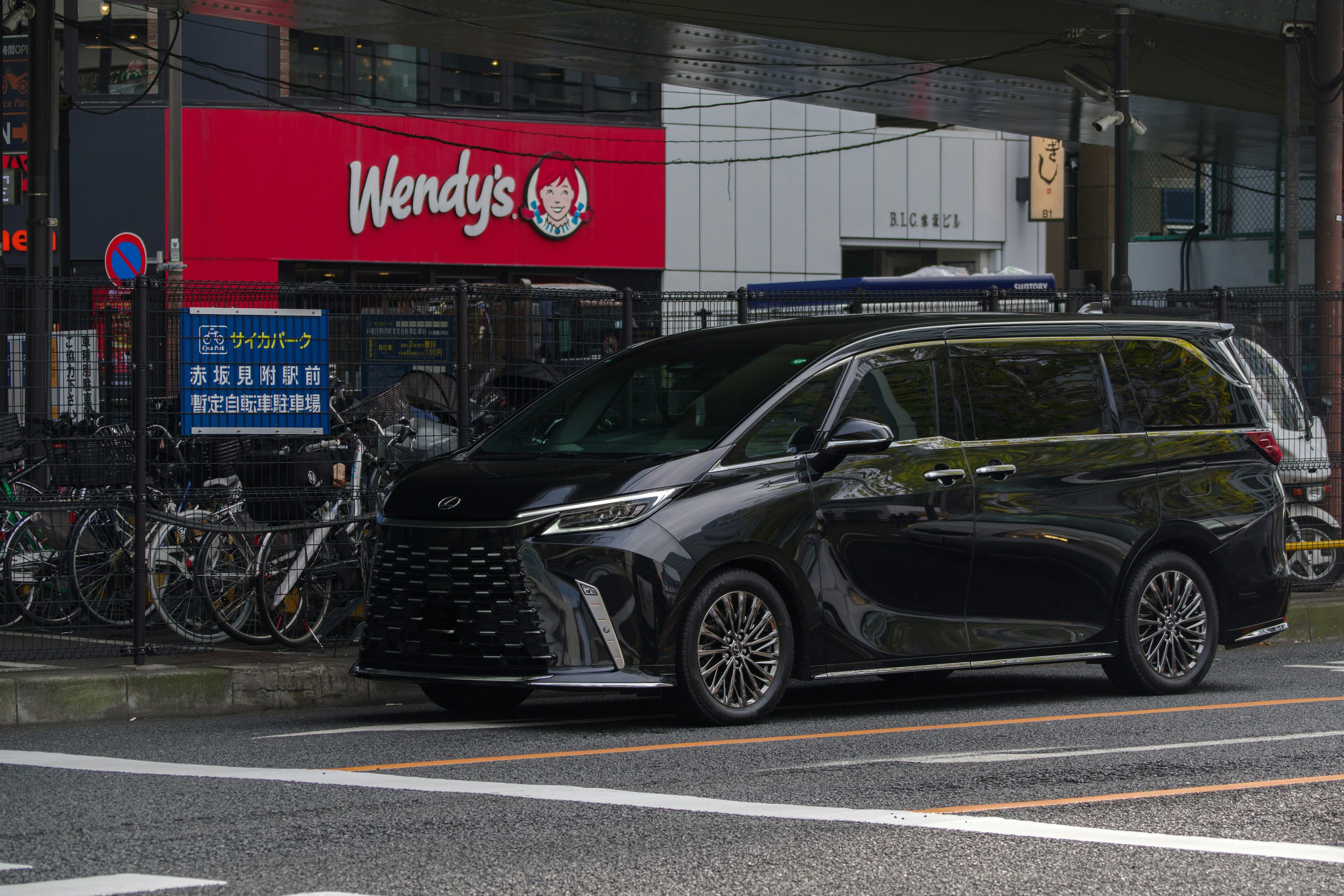 Minivan negro estacionado cerca de un restaurante Wendy's con bicicletas al fondo