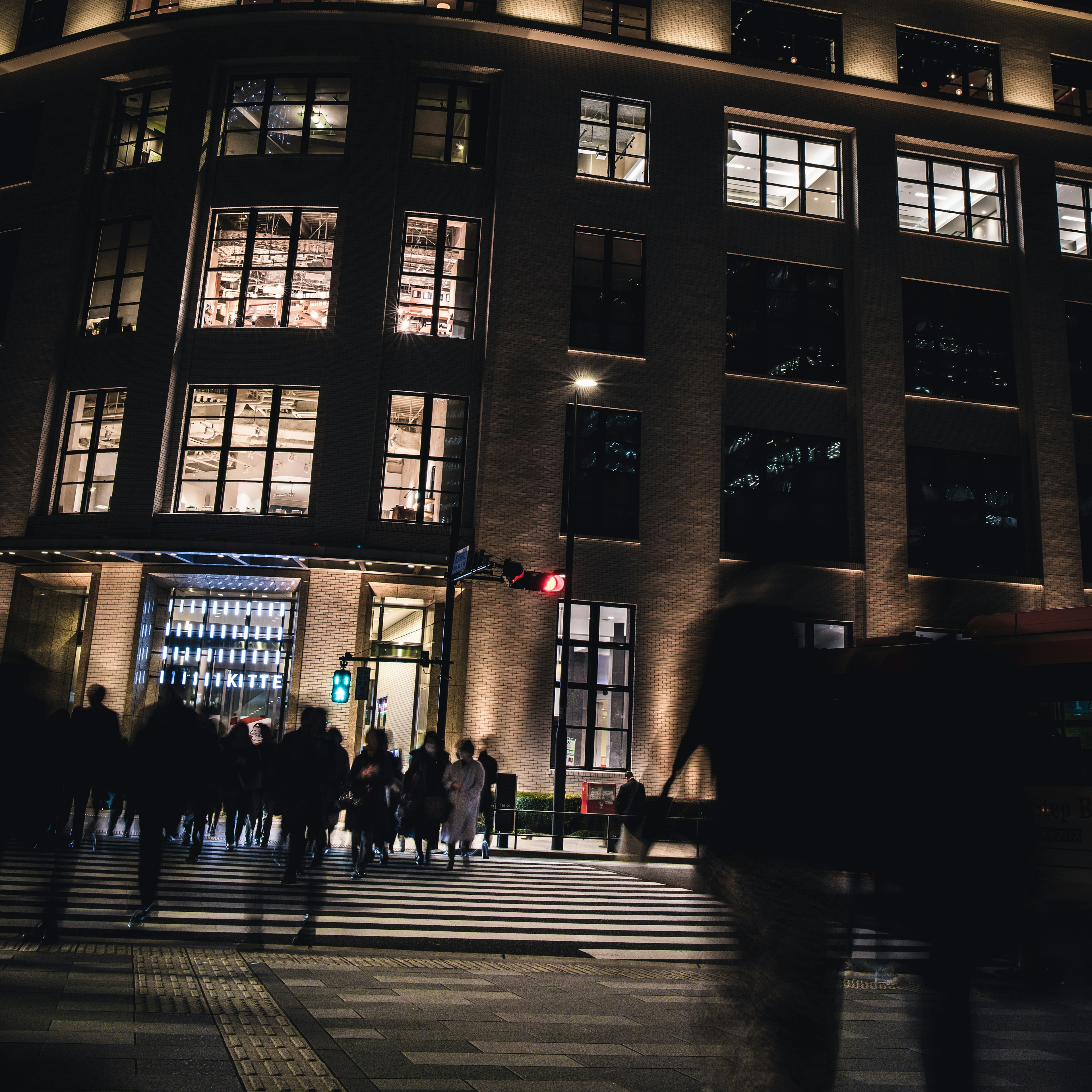 People crossing the street in front of a well-lit building at night