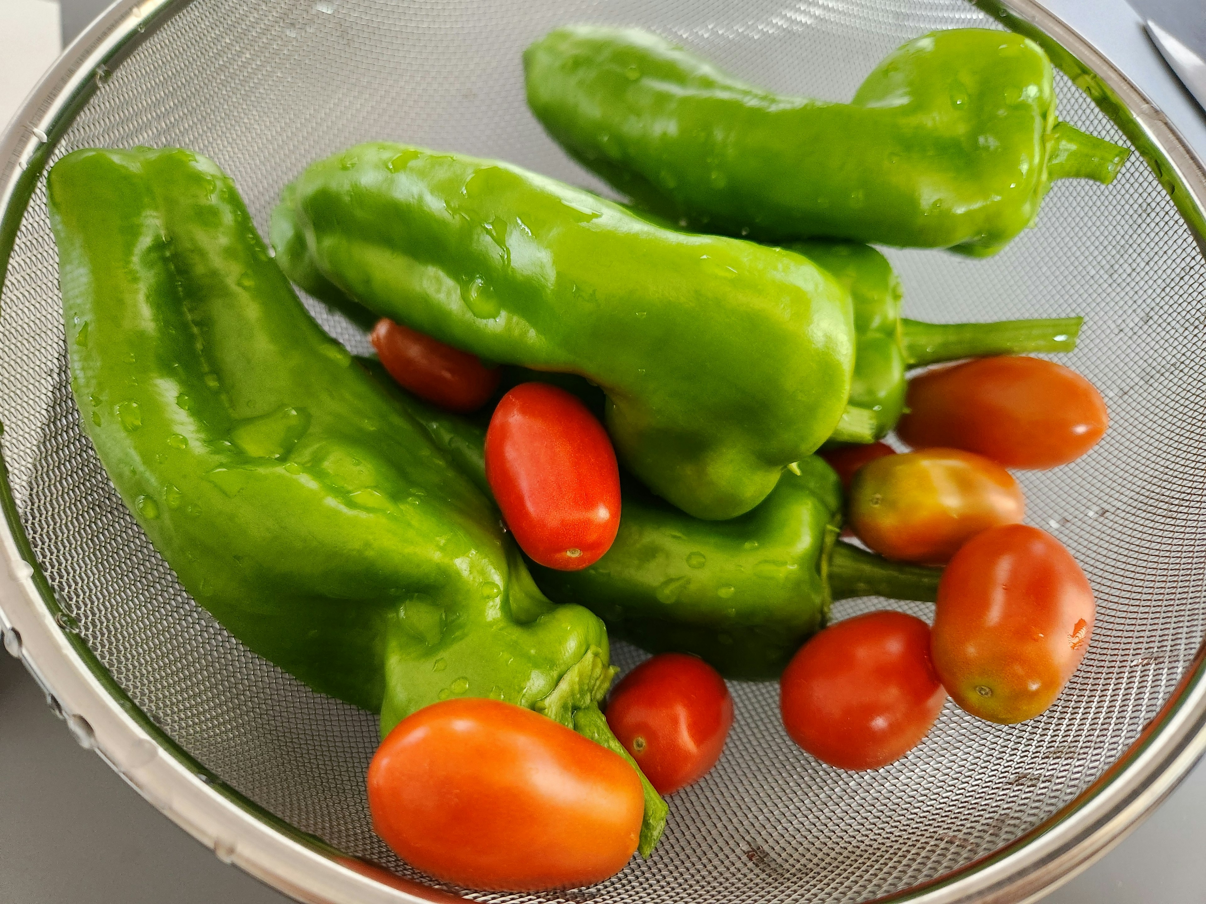 Green peppers and red cherry tomatoes in a colander