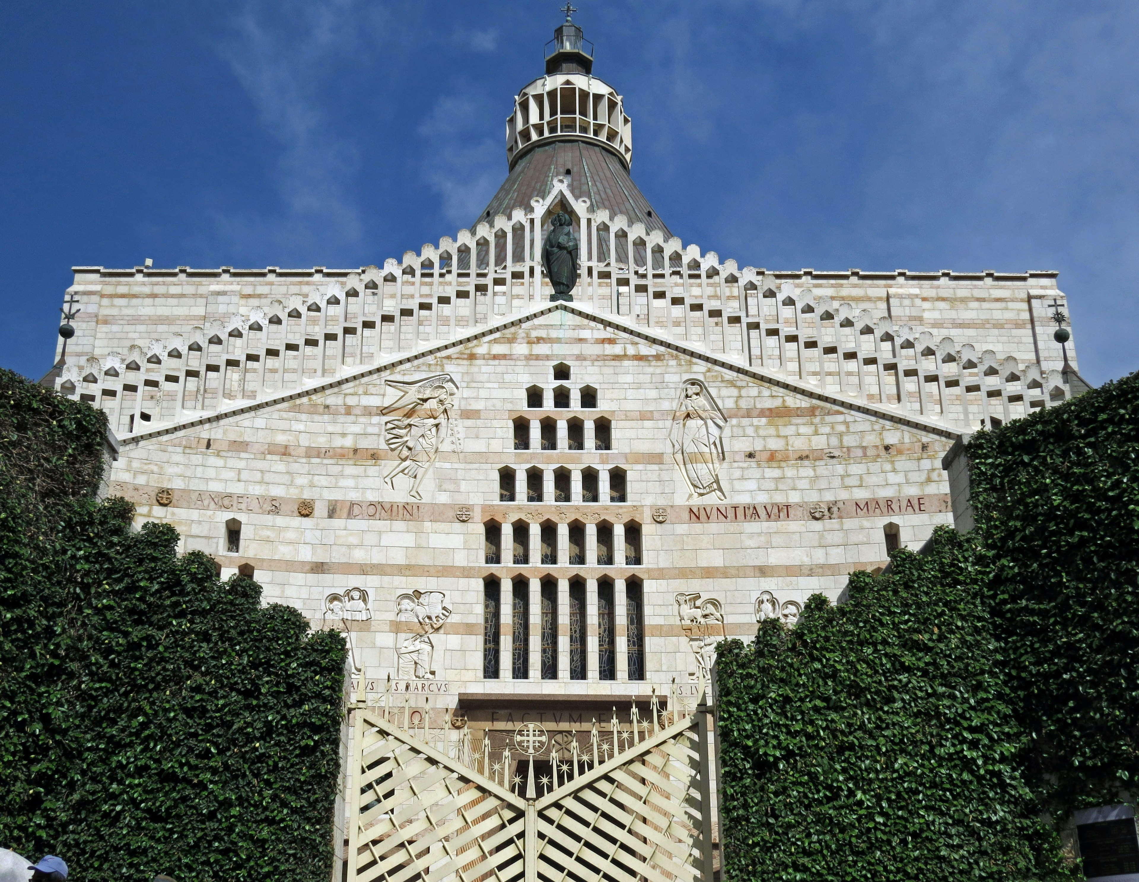 Stunning white stone building with intricate design surrounded by green plants and a large gate