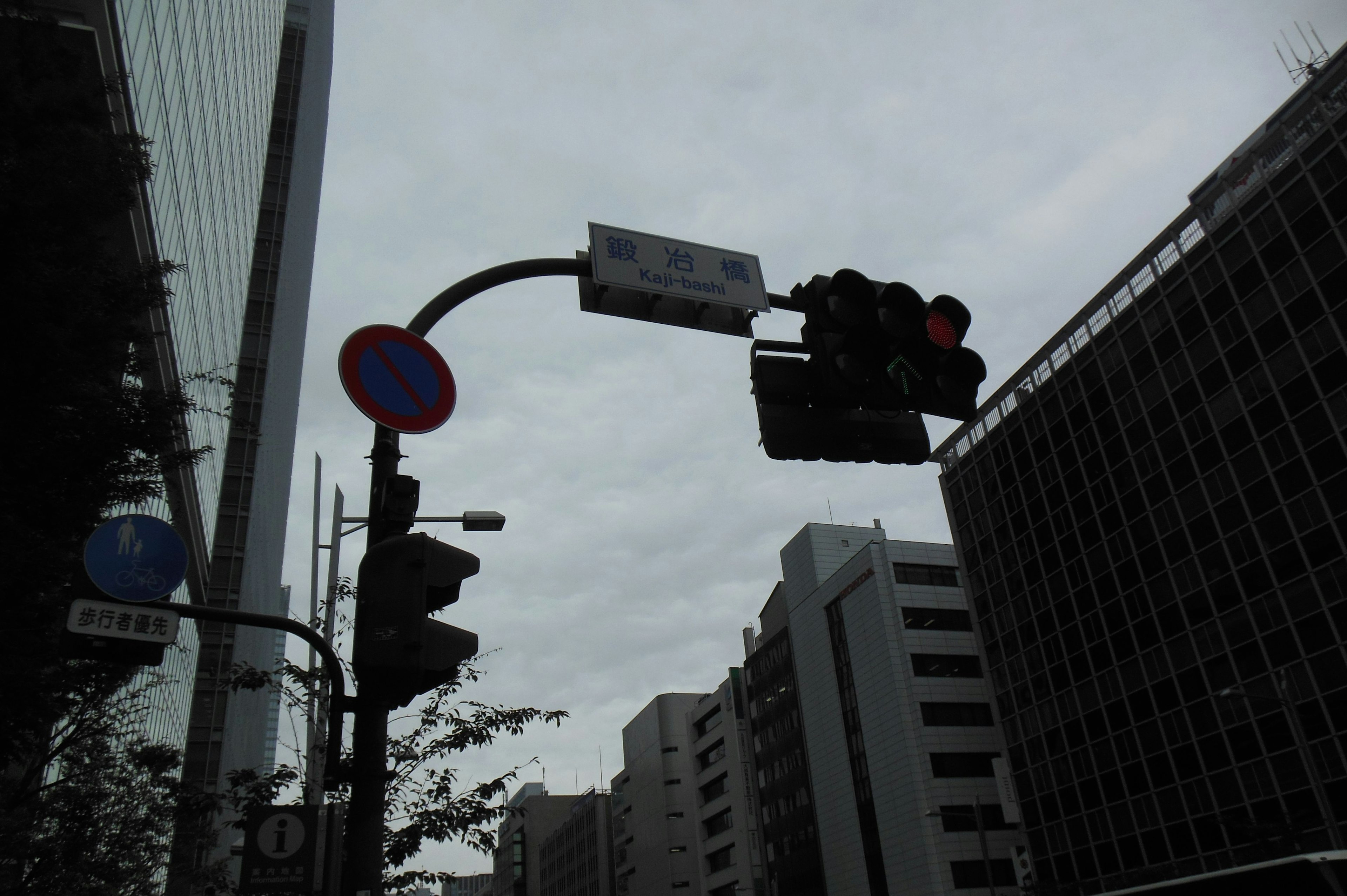 Pemandangan perkotaan dengan lampu merah dan tanda jalan biru di bawah langit mendung