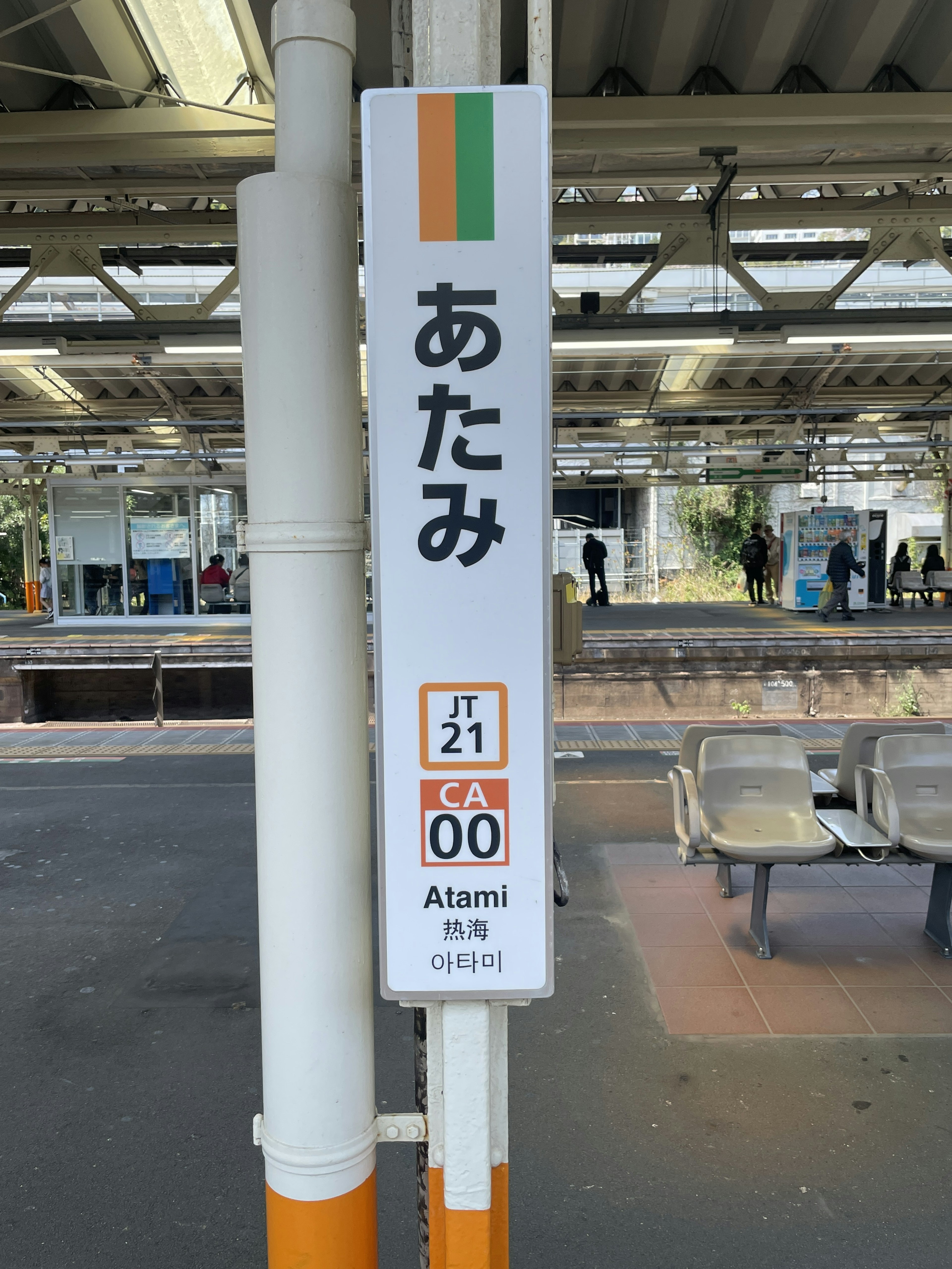 Insegna della stazione di Atami con caratteri giapponesi e informazioni sulla linea in design arancione e verde