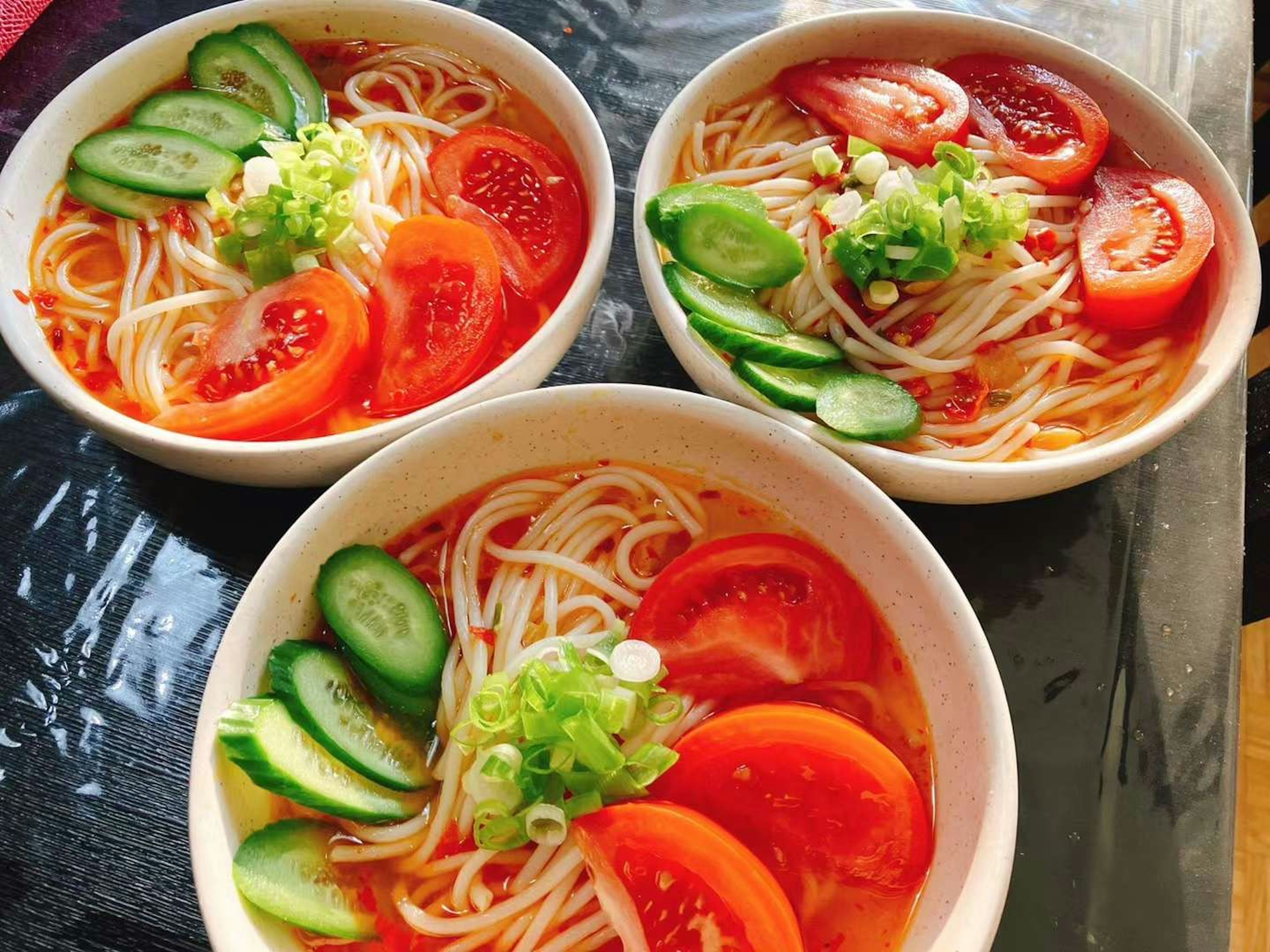 Tre ciotole di noodles freddi guarniti con fette di pomodoro e cetriolo fresco