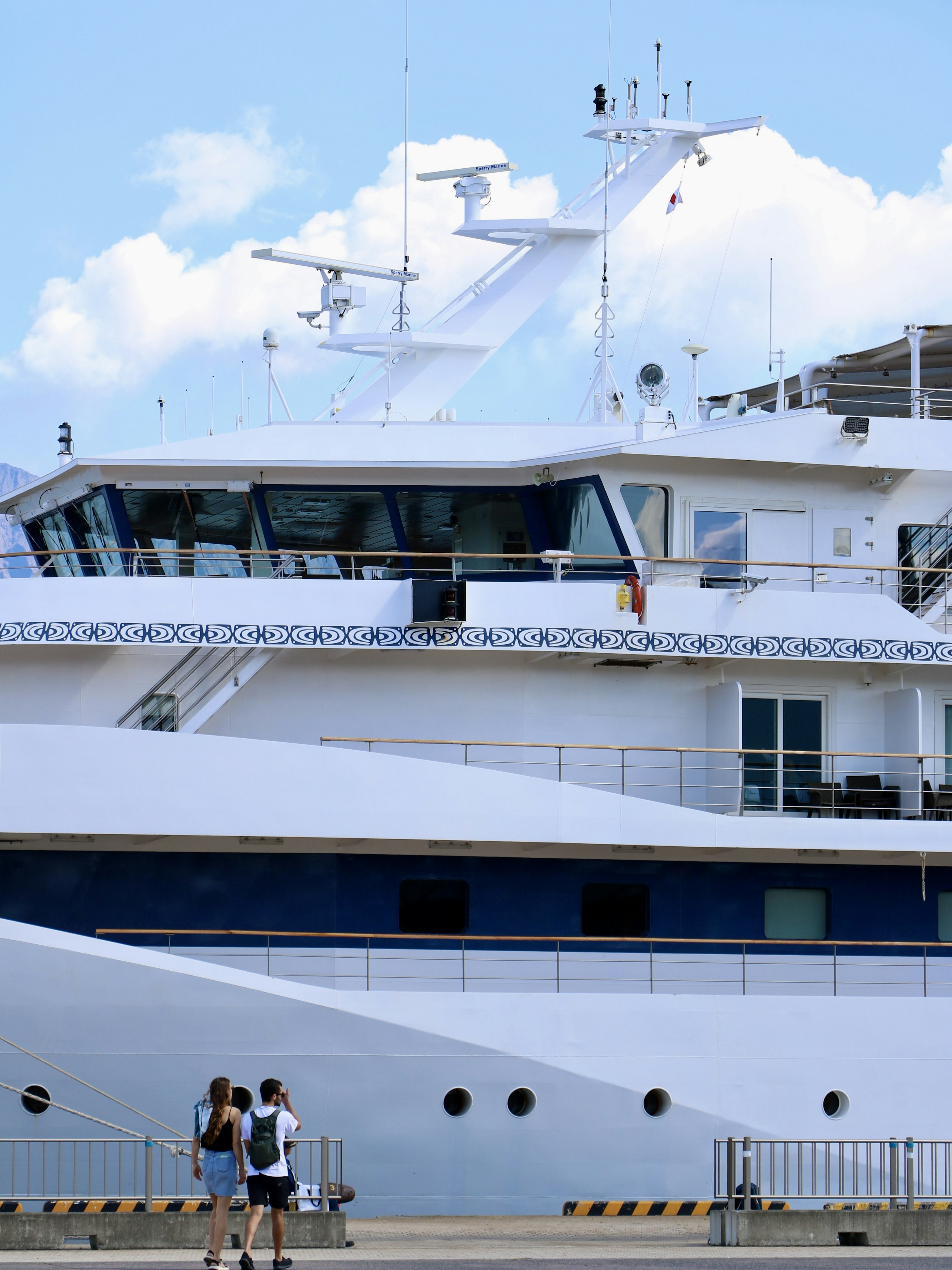 Side view of a large white cruise ship with two people standing nearby