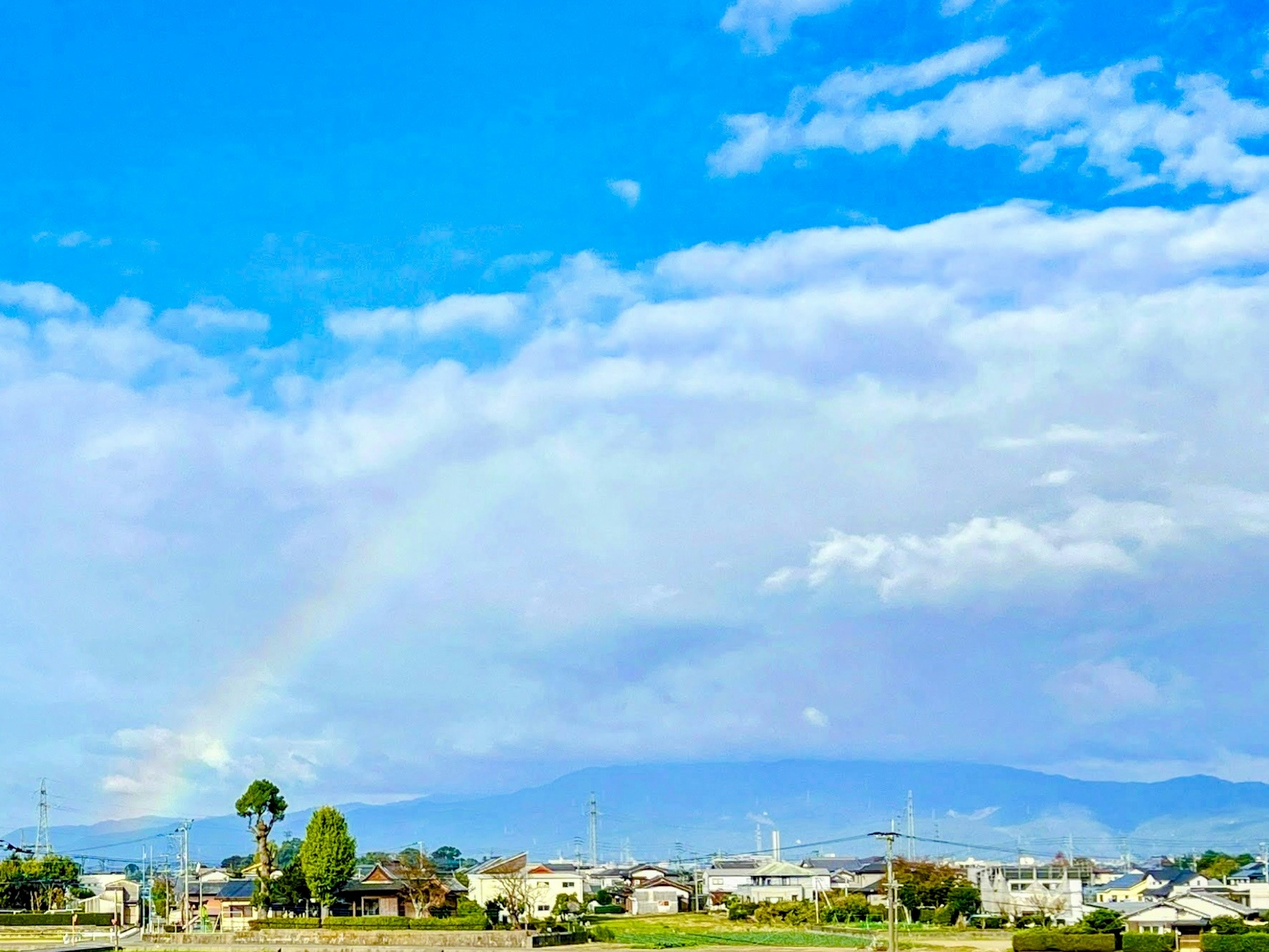 Landschaft mit einem Regenbogen unter einem blauen Himmel und Wolken