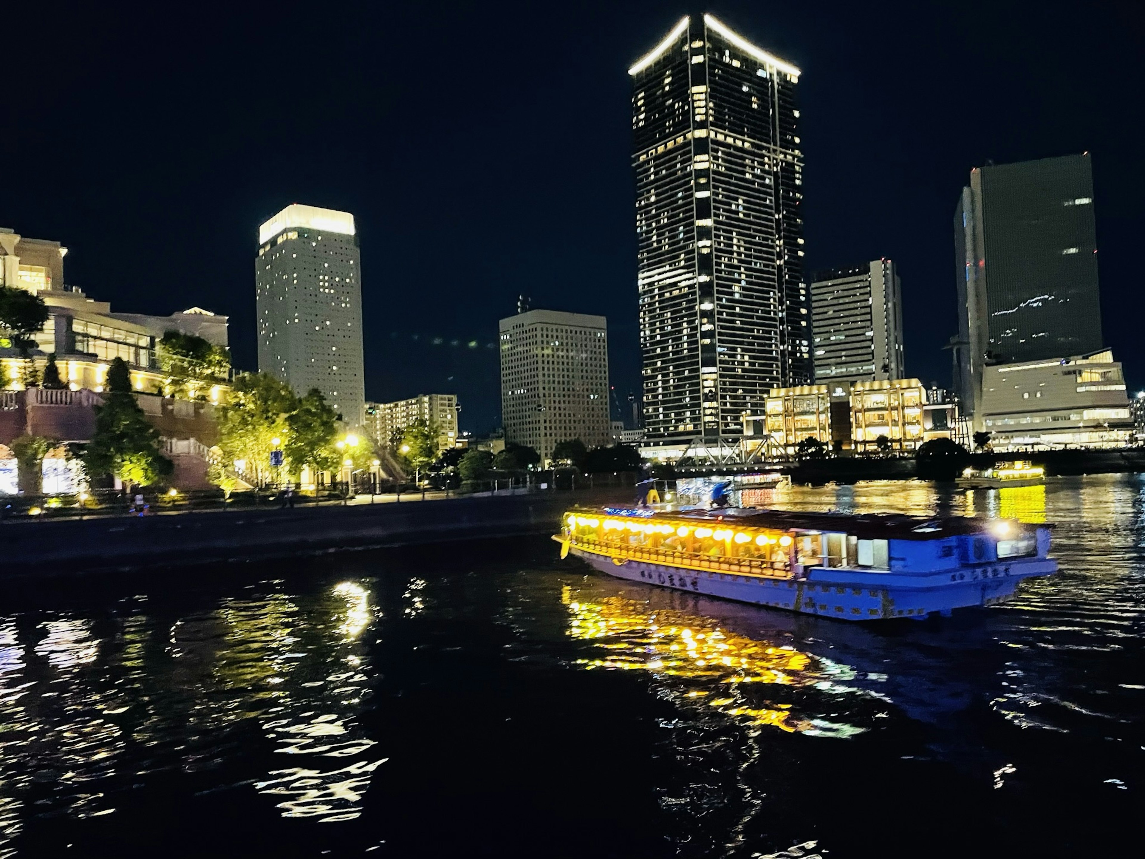 Bateau illuminé flottant sur la rivière avec des gratte-ciel dans le ciel nocturne