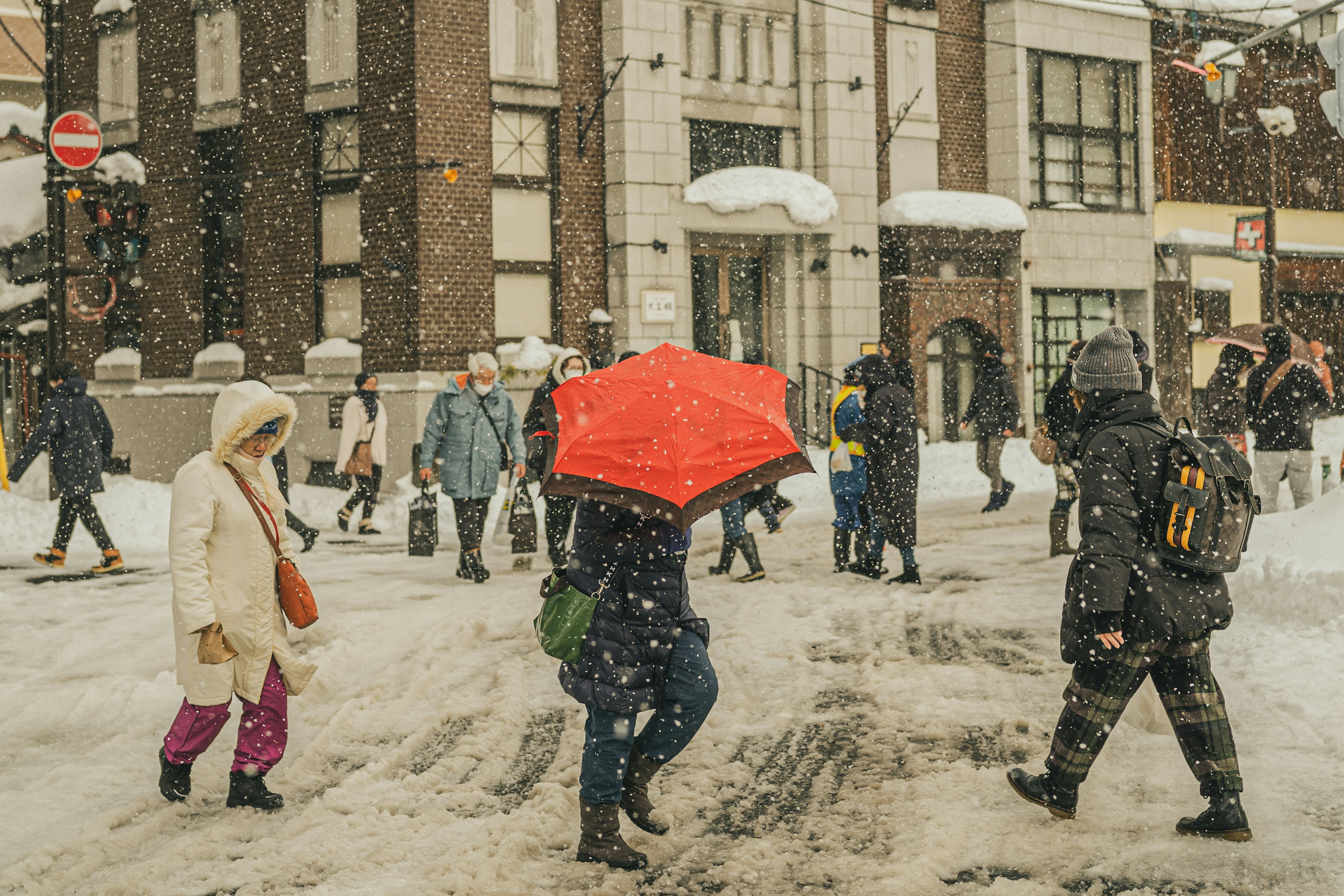 雪の中を歩く人々と赤い傘の女性