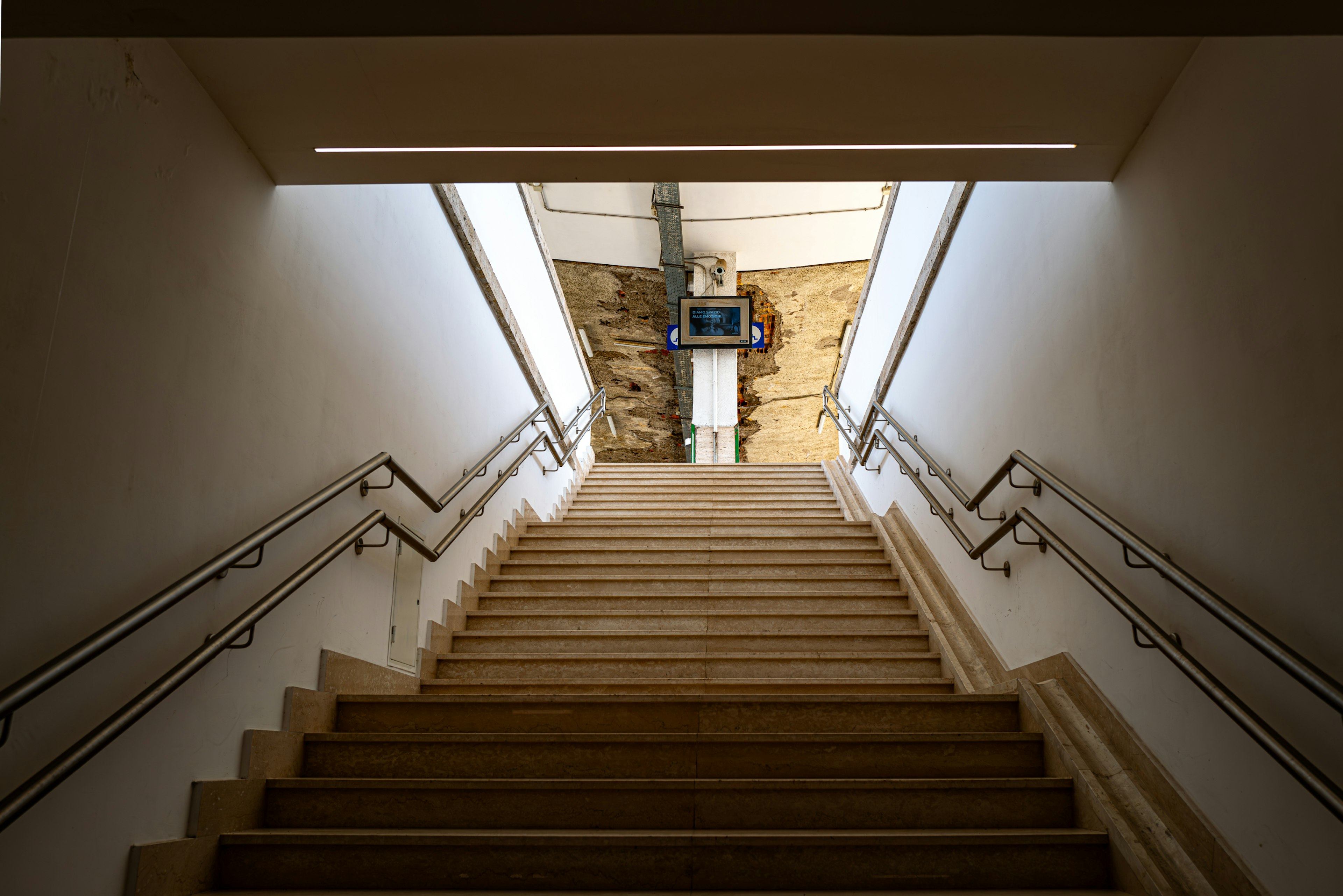 View from the top of stairs showing wooden steps and railings leading to a bright space