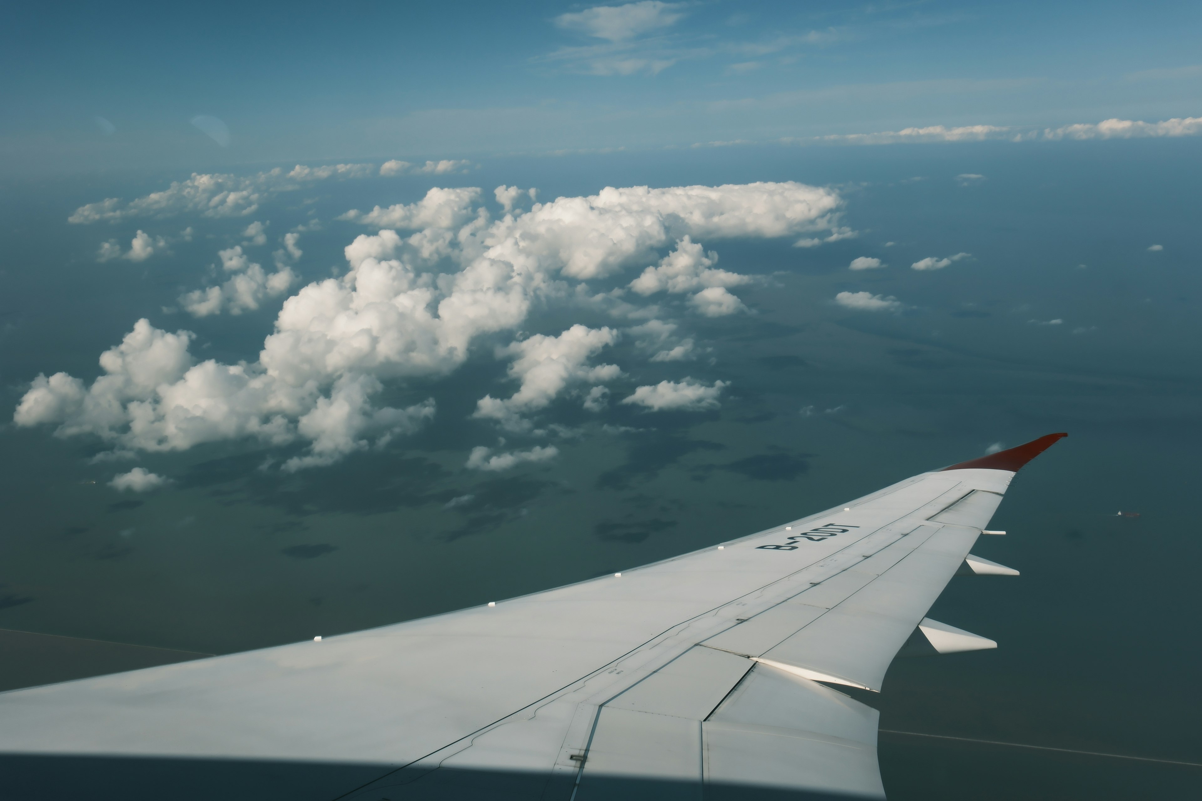 Vista del ala de un avión sobre el océano con nubes blancas esponjosas