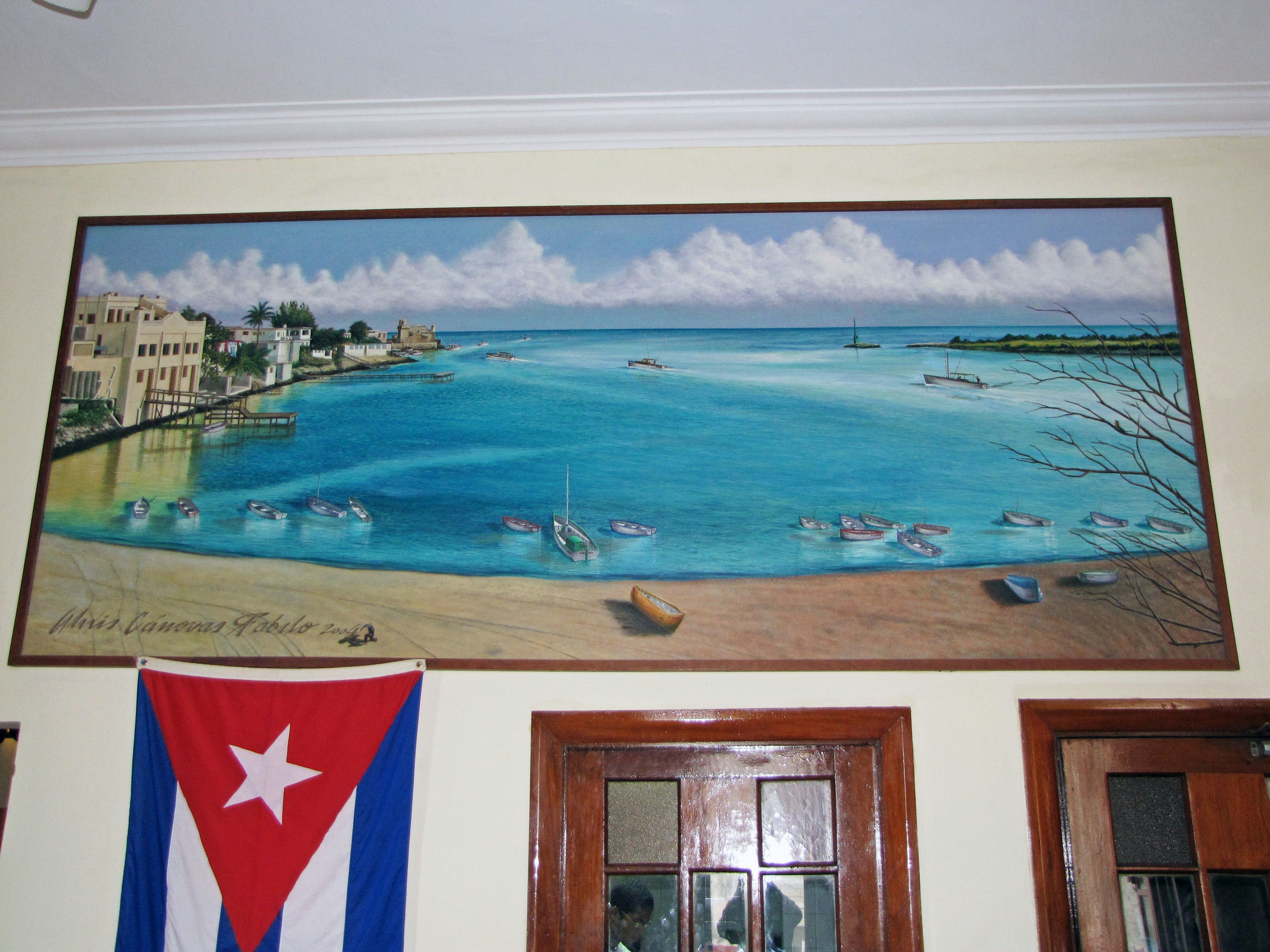 Large painting of a turquoise sea with white clouds hanging on the wall