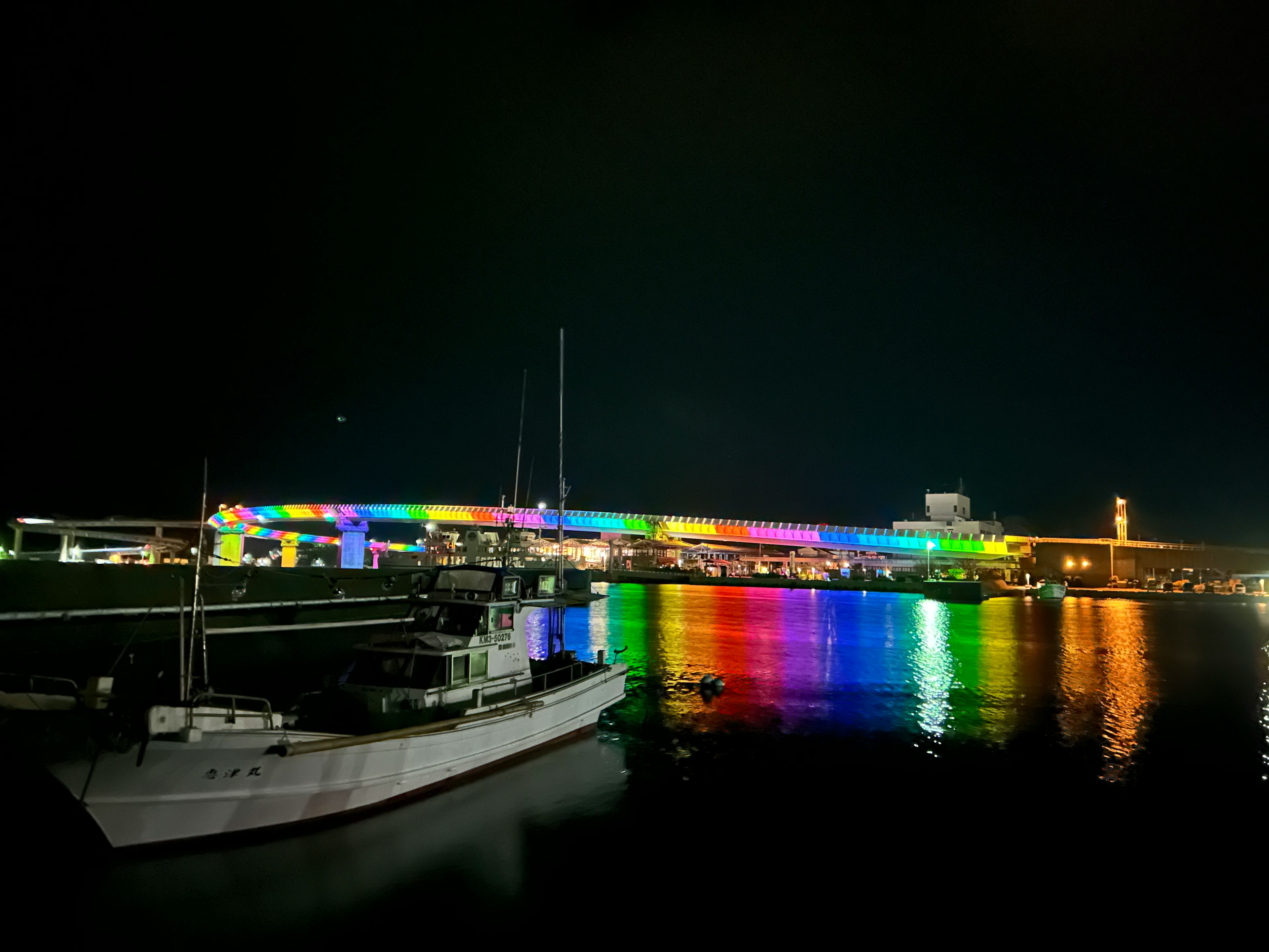 Una barca bianca in un porto di notte con luci colorate che si riflettono sull'acqua