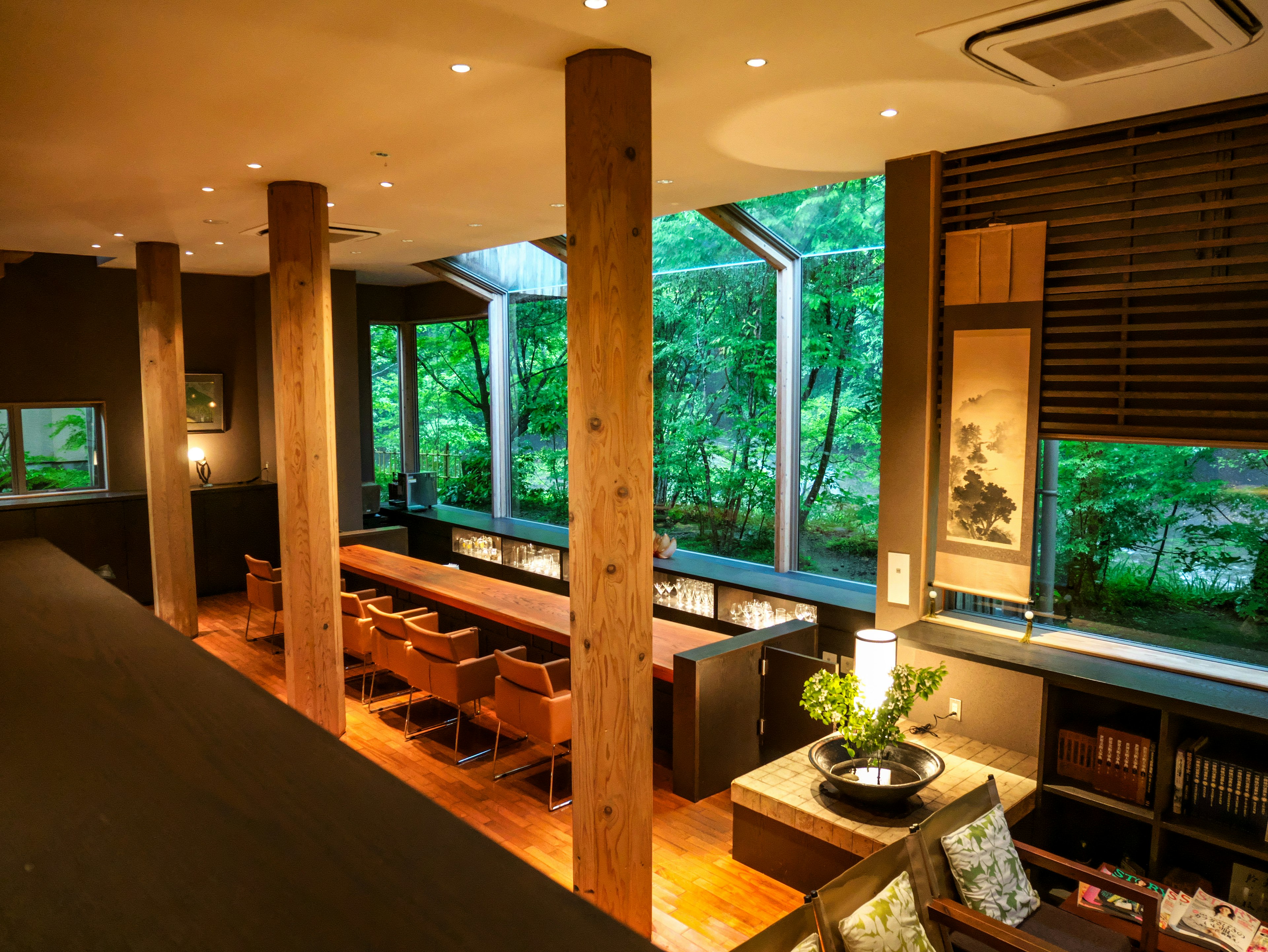 Interior de un café moderno con columnas de madera y grandes ventanales que muestran la vegetación