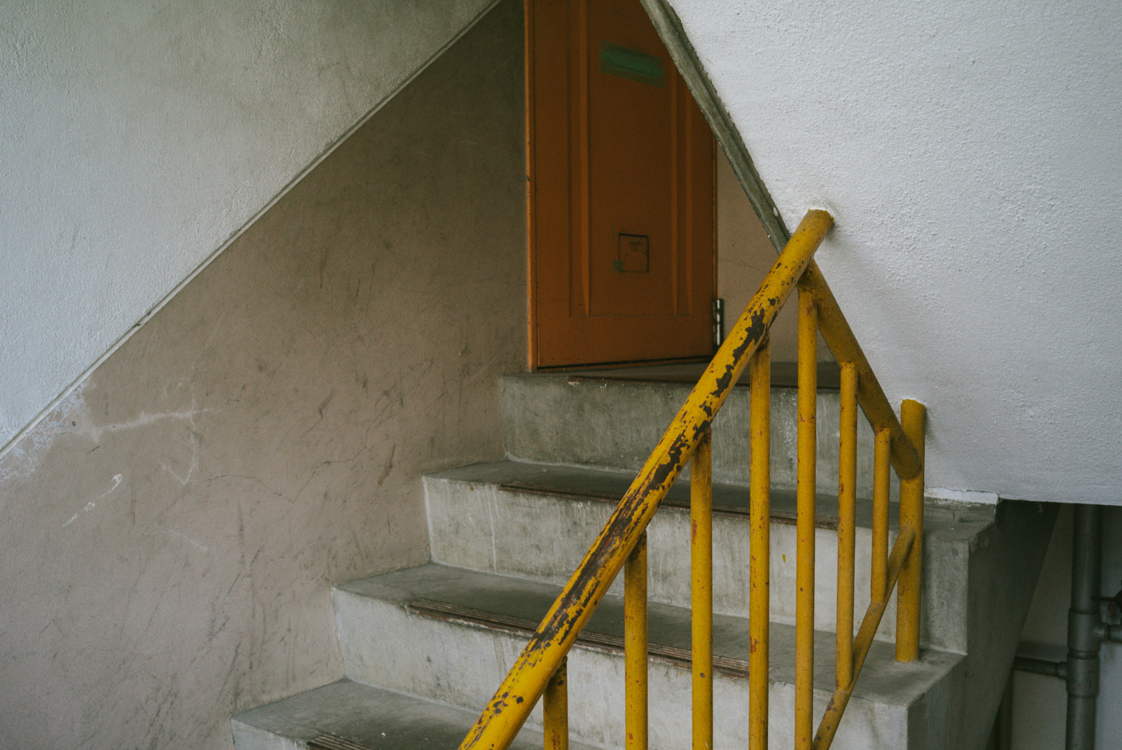 Escalier en béton avec une rampe jaune menant à une porte orange