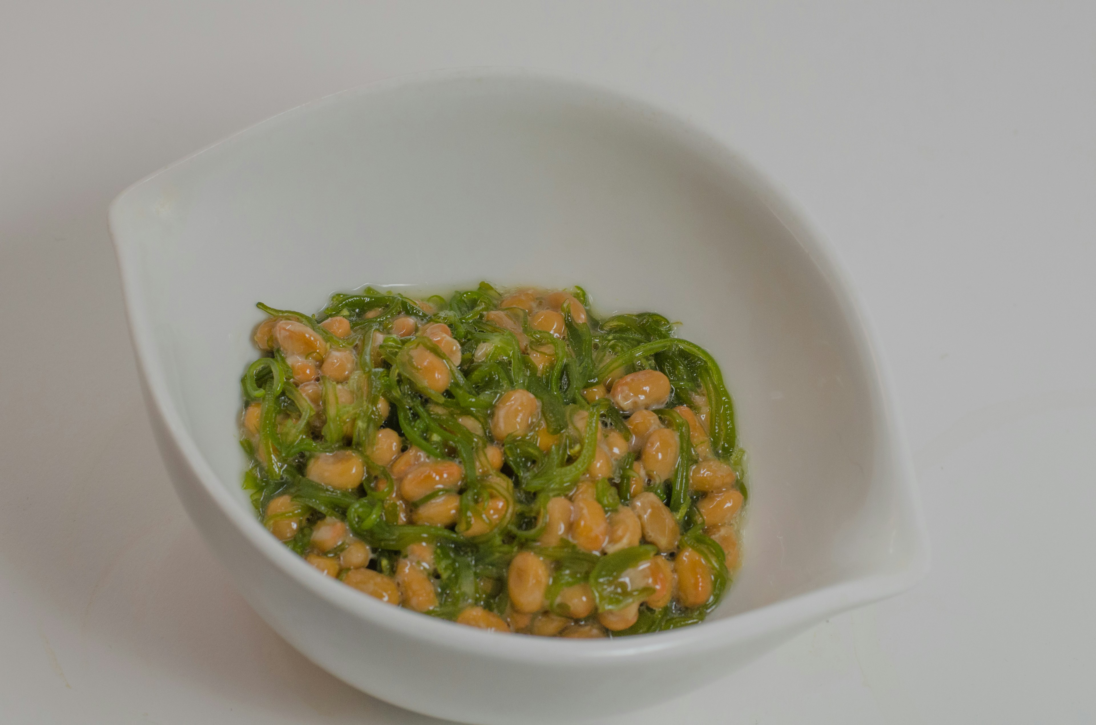 Dish of natto mixed with green vegetables in a white bowl