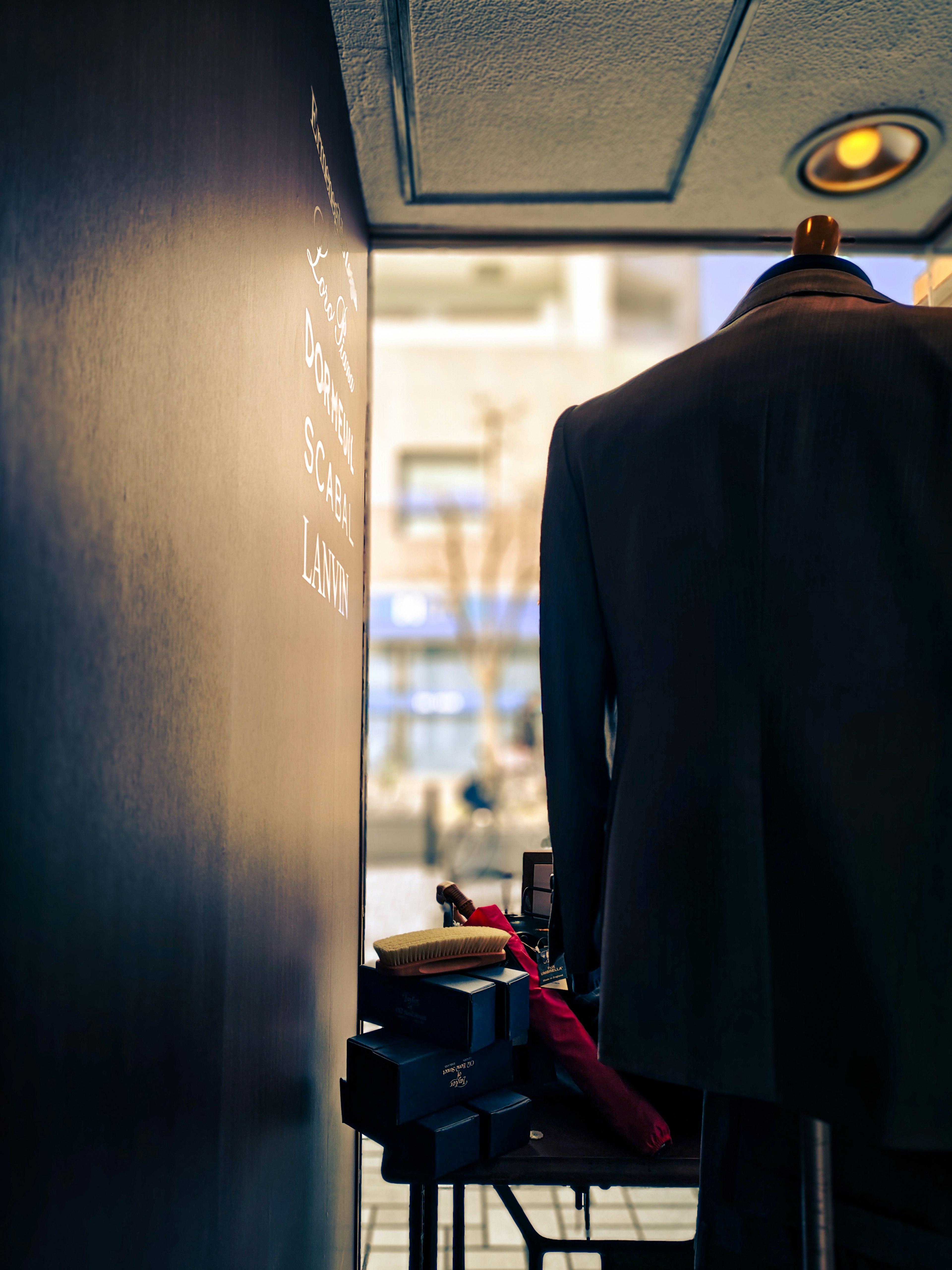 A mannequin wearing a suit in front of a black wall with clothing accessories on a table